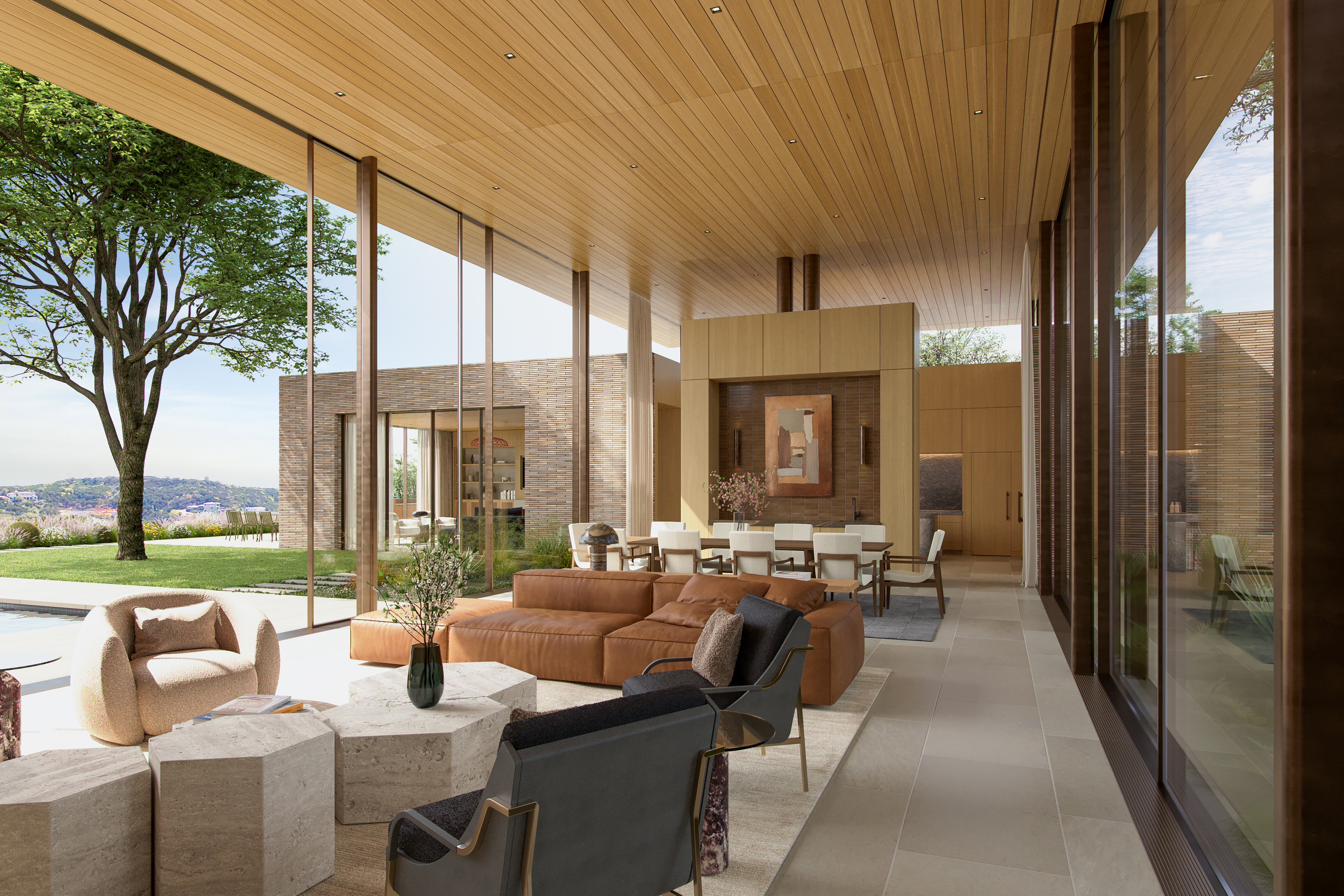 This luxurious living space boasts a seamless indoor-outdoor flow, characterized by floor-to-ceiling glass walls that capture an expansive view of the lawn and distant hills. The room features high-end contemporary furnishings, including a caramel leather sectional and textured accent chairs, all resting under a dramatic, wood-paneled ceiling. An integrated dining area with a stone fireplace creates a sophisticated and open-plan environment, perfect for modern living and entertaining.