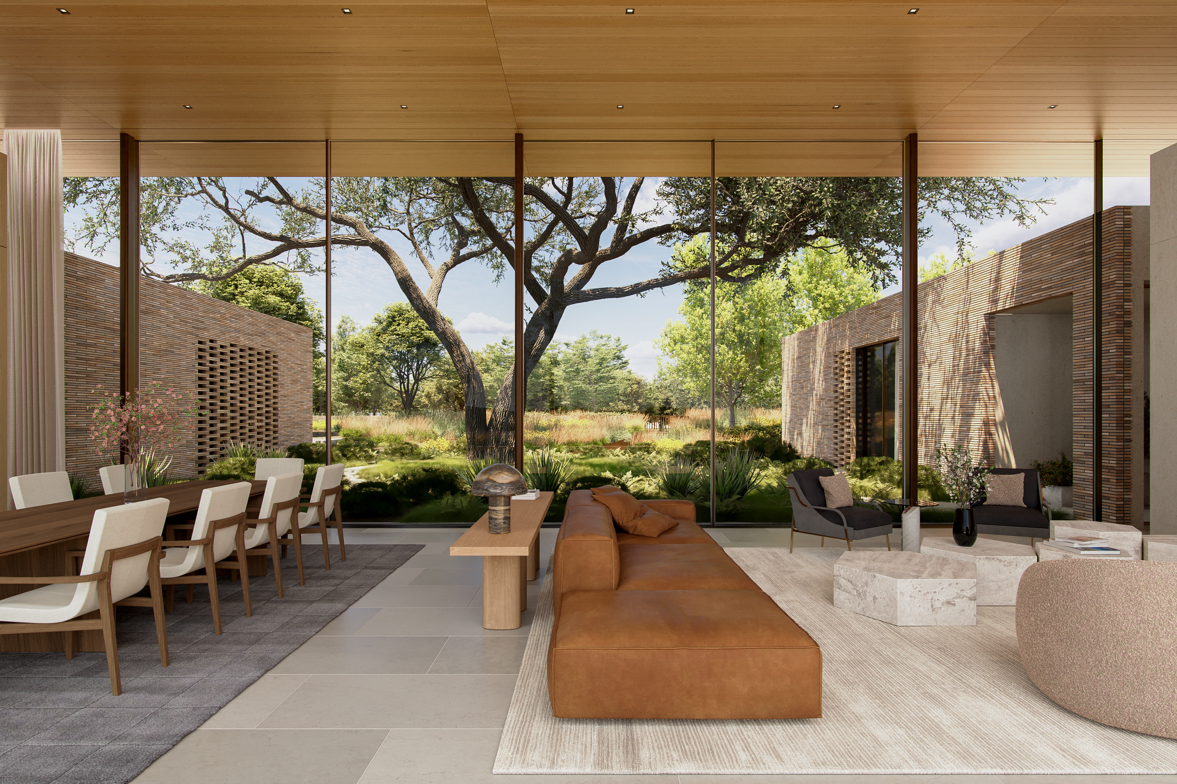 This stunning open-concept living and dining space features floor-to-ceiling glass walls that seamlessly integrate the outdoors with the home's sophisticated interior. The area is furnished with high-end modern pieces, including a cognac leather sectional, sculptural stone coffee tables, and a long wooden dining table, all set against a neutral, textural backdrop. The architectural design emphasizes natural materials and expansive views, creating a luxurious and tranquil atmosphere.