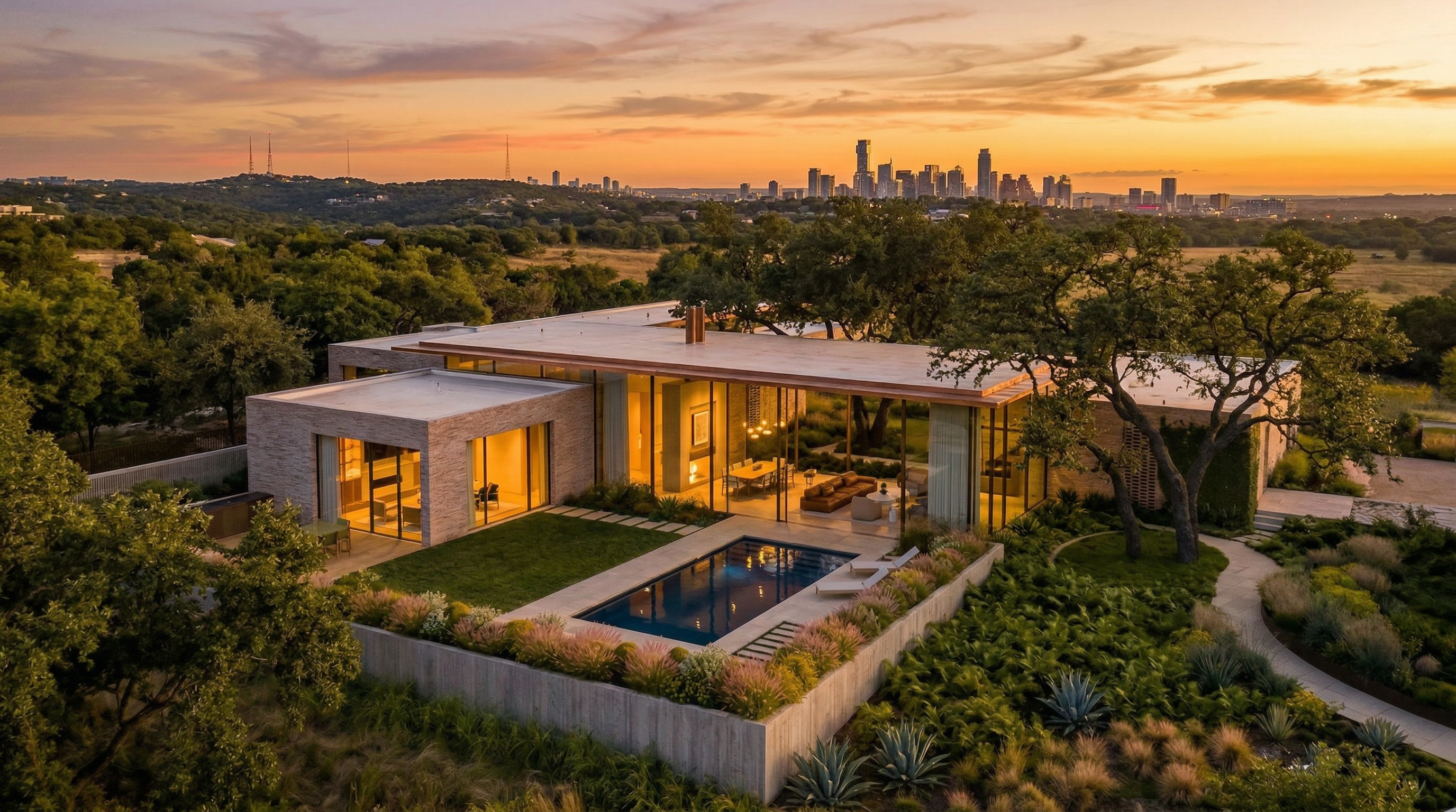 This stunning contemporary residence is captured in an expansive aerial view at sunset, highlighting its seamless integration with the natural landscape and unobstructed city skyline views. The home features a flat roofline, floor-to-ceiling glass walls, and a private pool set within a beautifully landscaped yard. The architectural style emphasizes clean lines and a sophisticated indoor-outdoor living experience.
