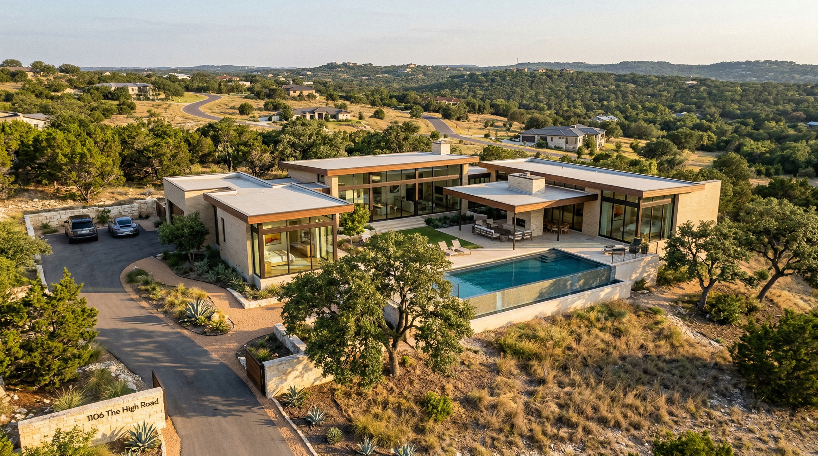 This stunning contemporary estate features a low-profile architectural design with extensive glass walls and natural stone accents, seamlessly blending into the surrounding hill country landscape. The property centers around an infinity-edge pool, multiple lounge areas, and a spacious outdoor patio, creating an ideal setting for luxury indoor-outdoor living. With a paved driveway, mature trees, and panoramic views of the hilly topography, the residence offers both privacy and a sophisticated modern aesthetic.