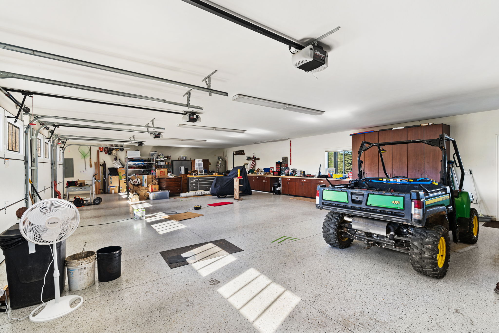 This spacious, well-organized three-car garage features a durable, speckled epoxy floor finish and high ceilings with dual overhead door openers. It offers ample storage, including built-in cabinetry and workbench areas, and currently houses an off-road utility vehicle, making it an ideal space for automotive storage or a hobby workshop.