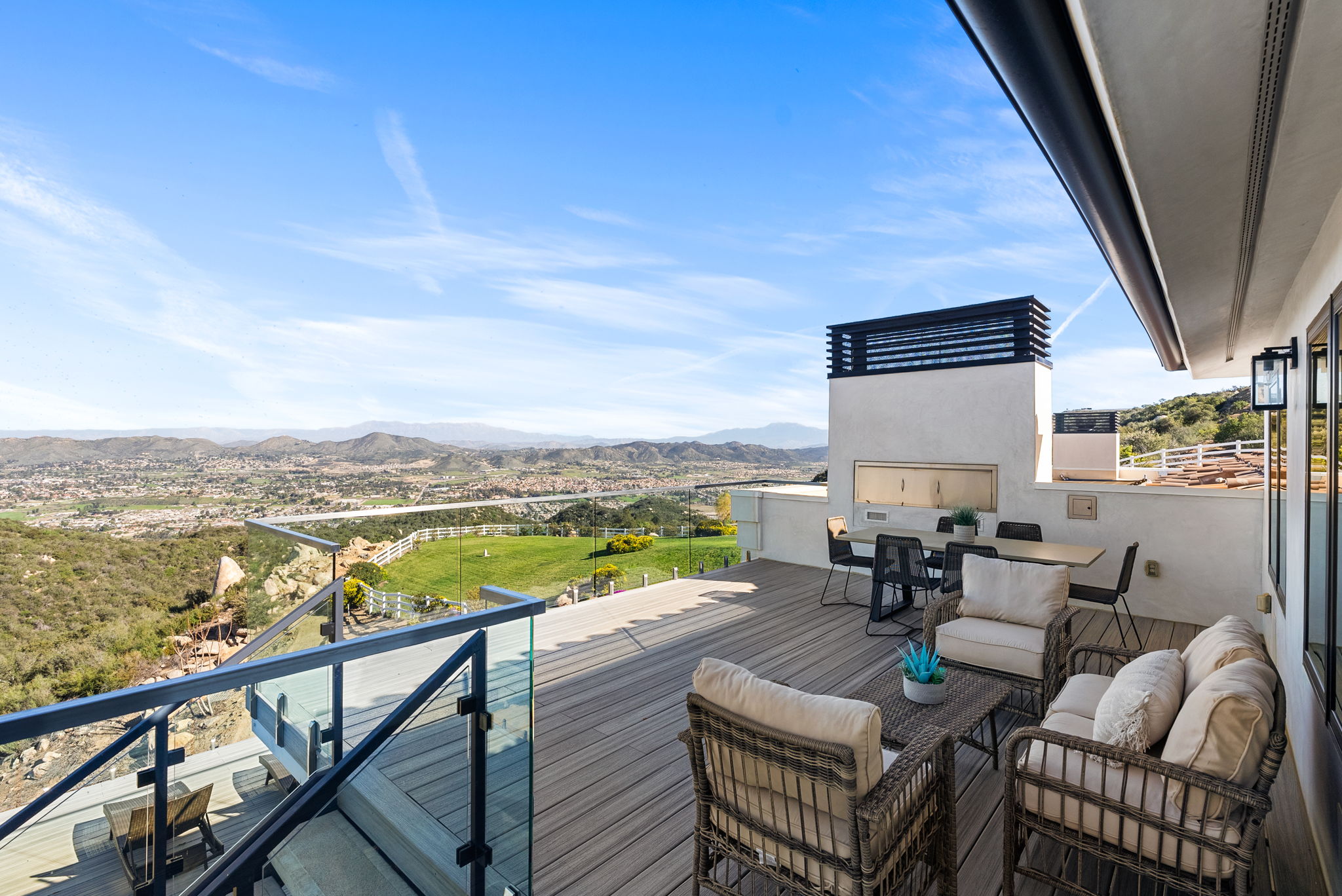 This expansive, multi-level deck offers a luxurious outdoor living space with breathtaking panoramic views of the surrounding hills and valley. The deck is well-appointed with comfortable wicker patio furniture, a sleek dining set, and a built-in outdoor fireplace, making it an ideal setting for entertaining. Its modern glass railing ensures unobstructed vistas, emphasizing the home's premier elevated location and sophisticated architectural design.
