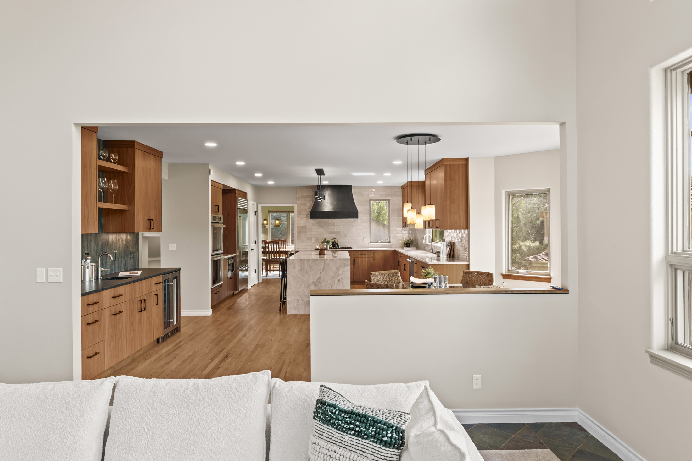 This interior shot showcases a modern kitchen with warm wood cabinetry and a contrasting dark range hood. The open-concept design allows for seamless flow into the adjacent living space, creating an inviting atmosphere. Natural light streams in through the windows, highlighting the clean lines and contemporary finishes.
