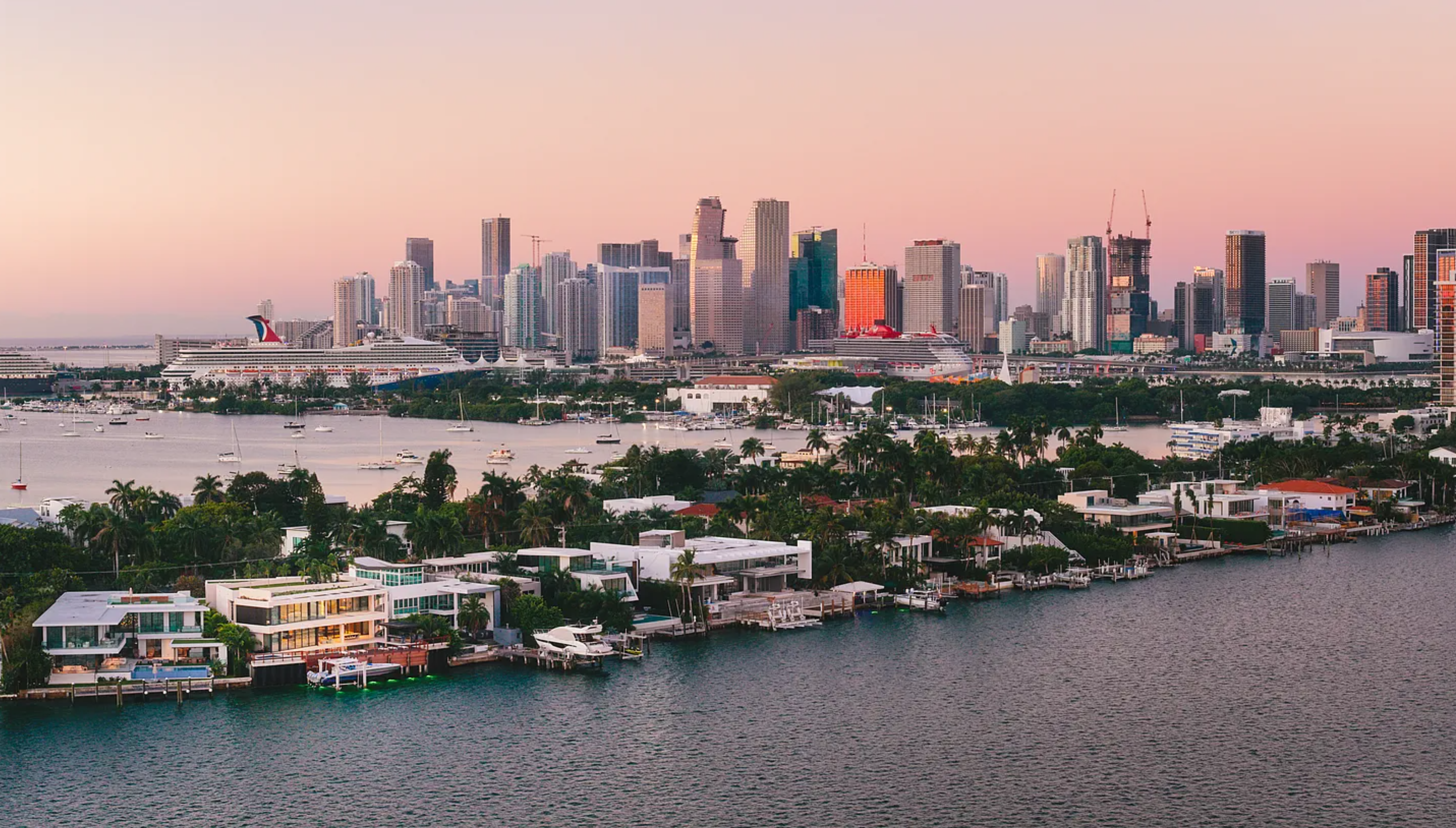 This aerial view showcases luxurious waterfront homes with modern architectural designs. Lush tropical landscaping surrounds the properties, enhancing their privacy and appeal. The waterfront location offers direct access to the water, with yachts and boats docked at private piers.