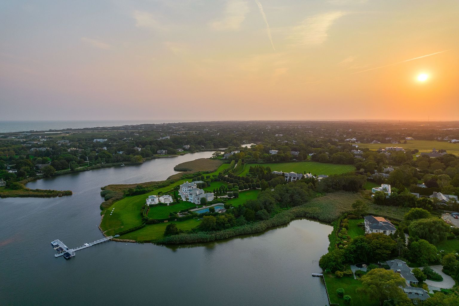 This aerial view showcases an expansive waterfront property featuring a large, luxurious home with manicured lawns and gardens. The property includes a private dock and is surrounded by water on multiple sides, offering stunning views and privacy. The overall impression is one of opulence and tranquility, ideal for a high-end real estate listing.
