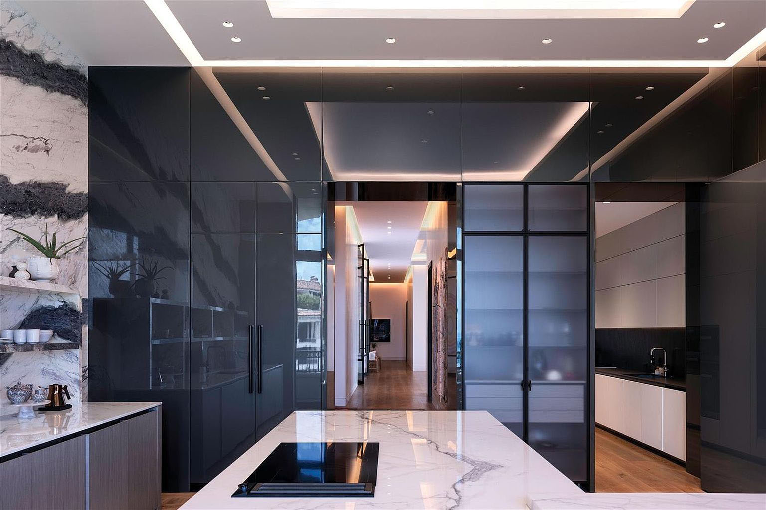 This image showcases a modern, high-end kitchen with sleek, dark cabinetry and stunning marble countertops. The space features an induction cooktop on the island and is accented by unique patterned wall details. The design emphasizes clean lines and sophisticated finishes, creating a luxurious and functional culinary space.