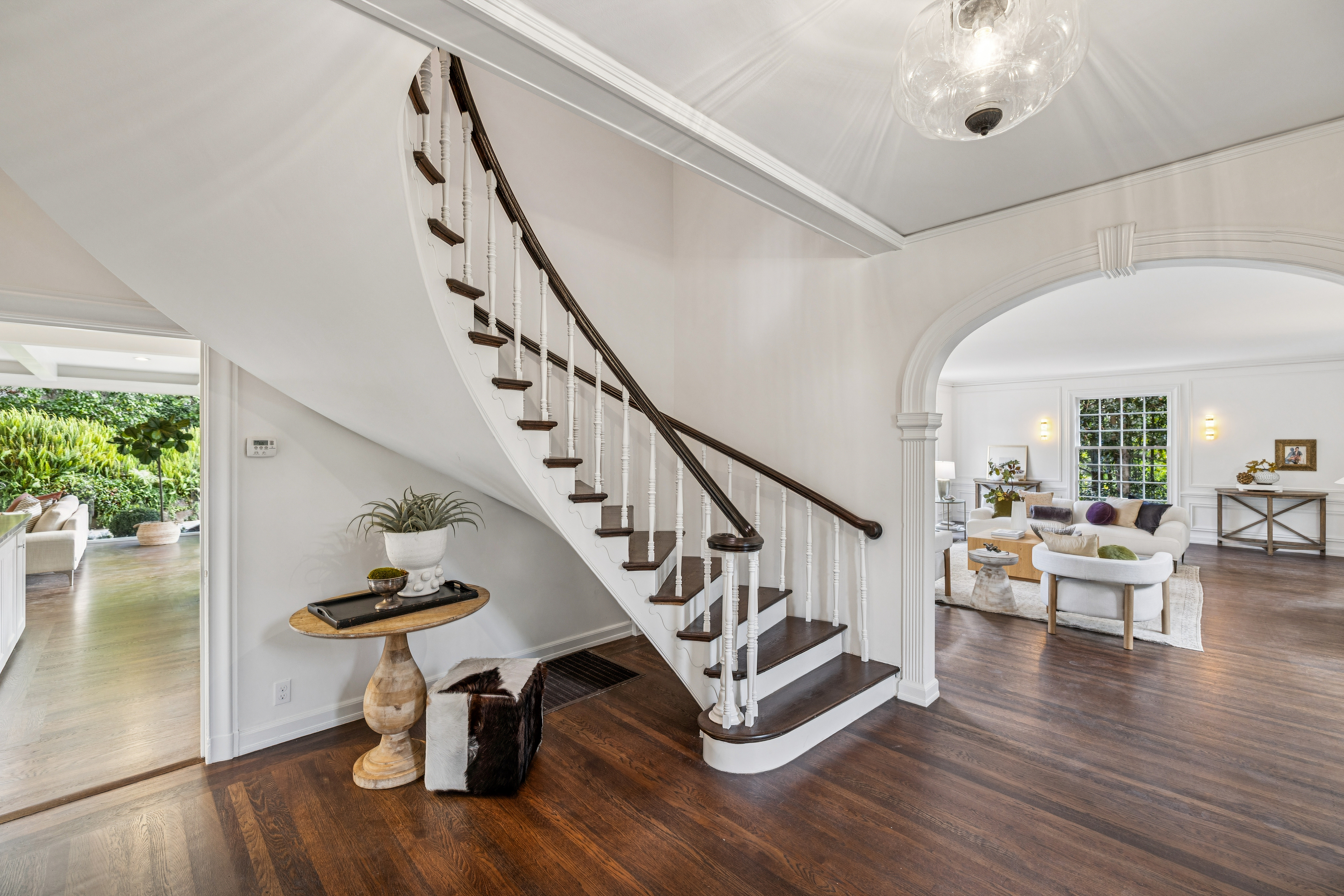 This interior shot showcases a grand hallway with a curved staircase, featuring dark wood treads and a white balustrade. The hardwood flooring adds warmth, while the white walls and trim create a bright and elegant atmosphere. An arched doorway leads to a living area, enhancing the home's flow and design.