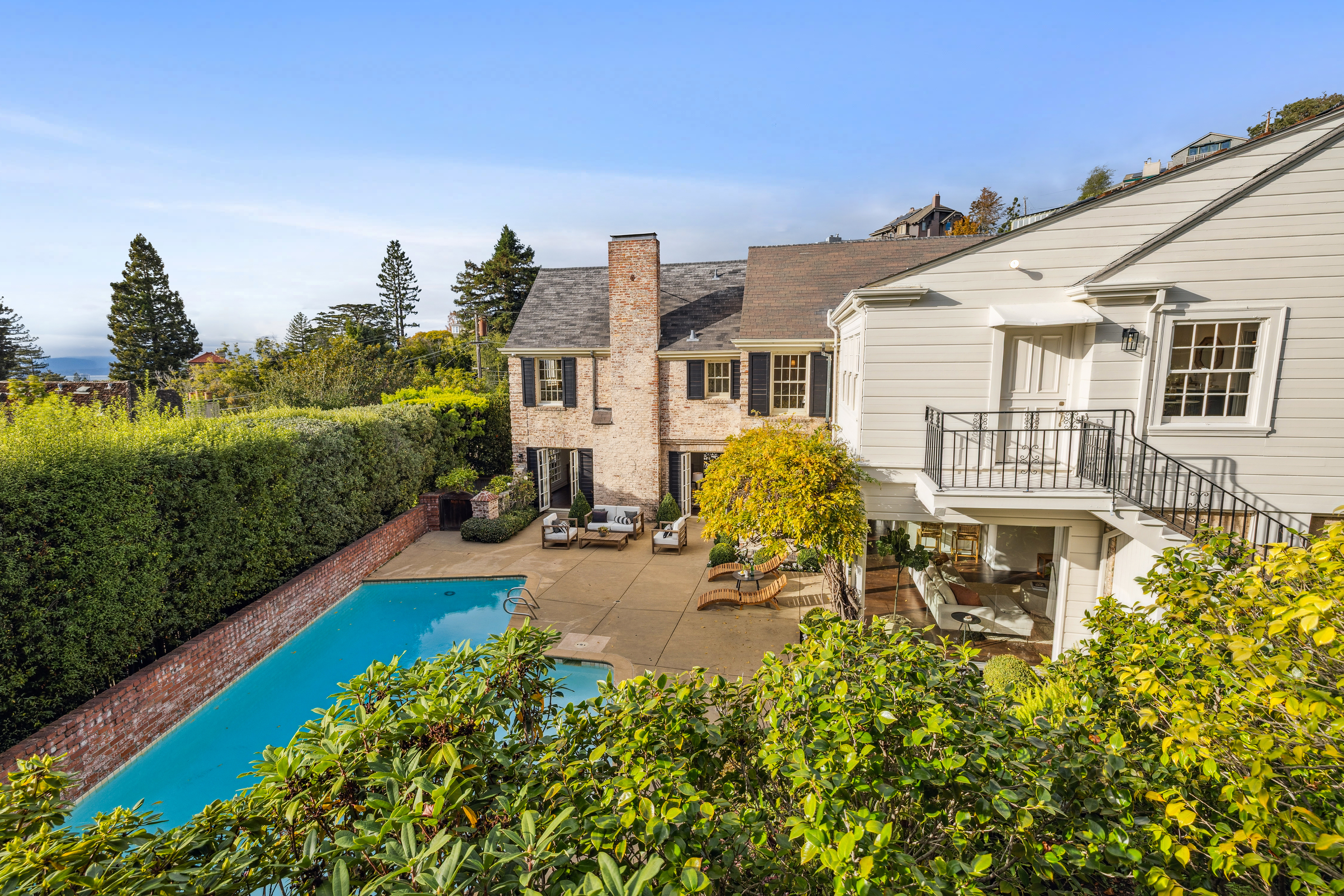 This image showcases the rear exterior of a stately home, featuring a brick facade, a well-maintained pool, and a spacious patio area with outdoor seating. The property is surrounded by lush greenery, providing privacy and a serene atmosphere. The architectural style blends classic elegance with modern outdoor living.