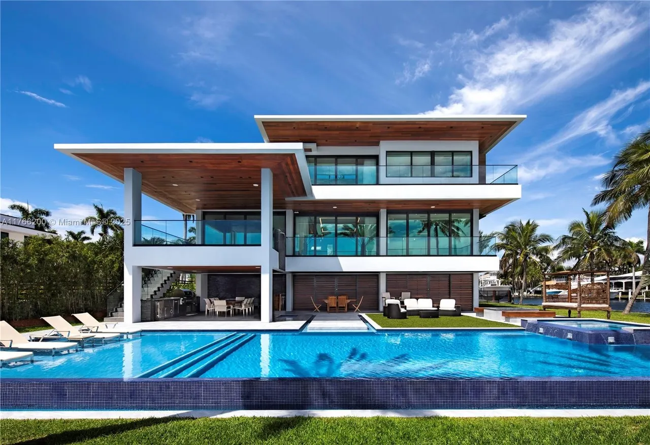 This image showcases a luxurious modern home with a stunning pool and spa area. The multi-level house features clean lines, large windows, and wooden accents, creating a sophisticated and inviting atmosphere. The pool is surrounded by well-manicured grass and lounge chairs, perfect for relaxation and entertainment.