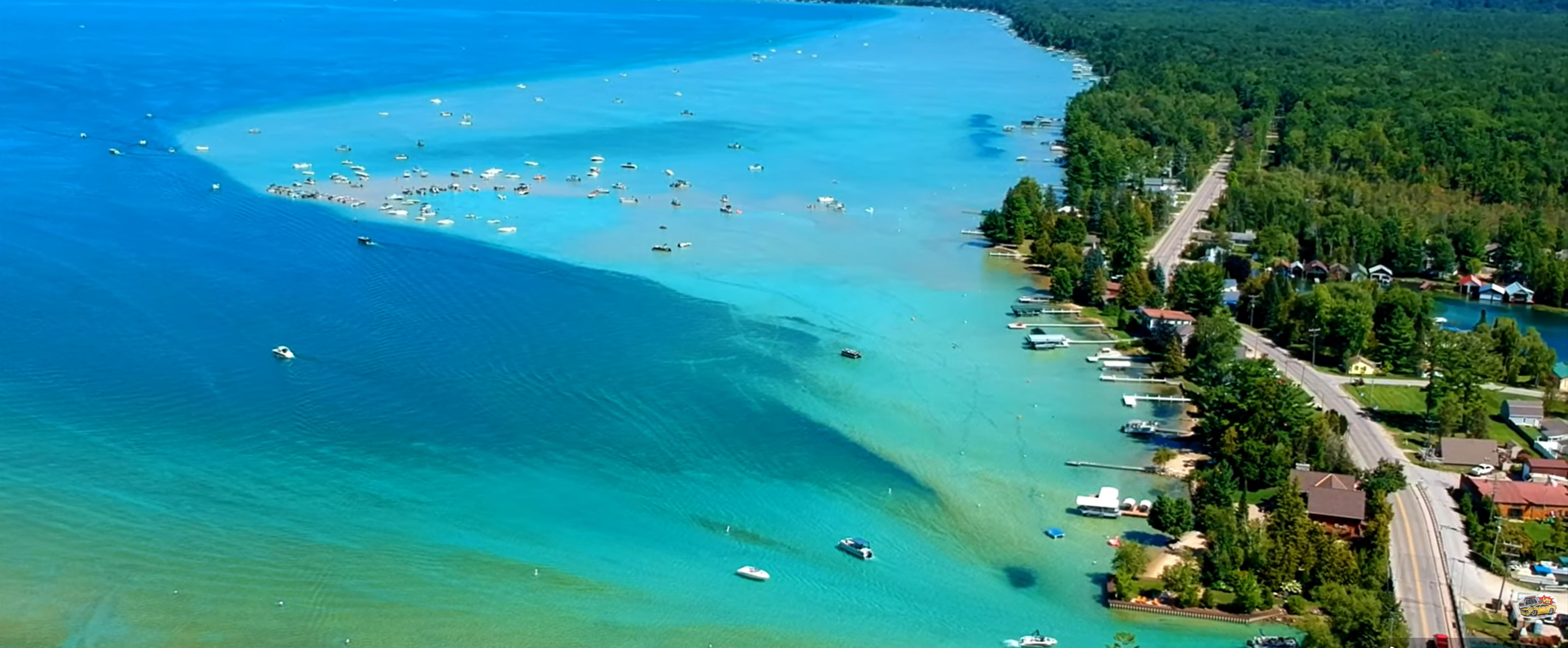 This aerial view showcases a picturesque waterfront property. The expansive property features direct access to a clear, turquoise body of water with several boats, suggesting recreational opportunities. Lush greenery surrounds the homes, enhancing privacy and natural beauty, while a nearby road provides easy access to the community.