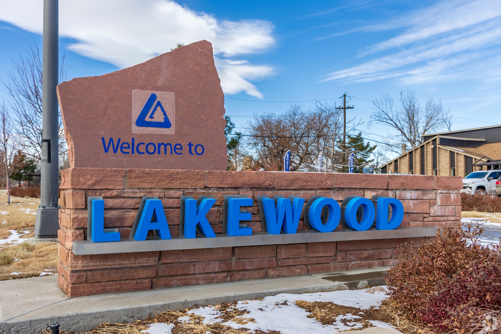 This image showcases the welcome sign for Lakewood. The sign features a stone structure with 'Welcome to' inscribed at the top along with the city's logo, and 'Lakewood' displayed in large, blue, block letters. The presence of snow suggests a winter setting, adding a touch of seasonal charm.