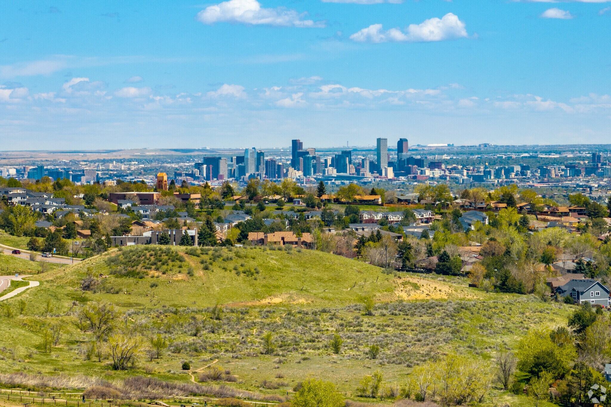 This aerial view showcases a tranquil neighborhood with well-maintained homes and lush greenery. The city skyline, including prominent skyscrapers, creates a striking backdrop. The setting presents a peaceful residential environment with convenient access to urban amenities, ideal for prospective homeowners.