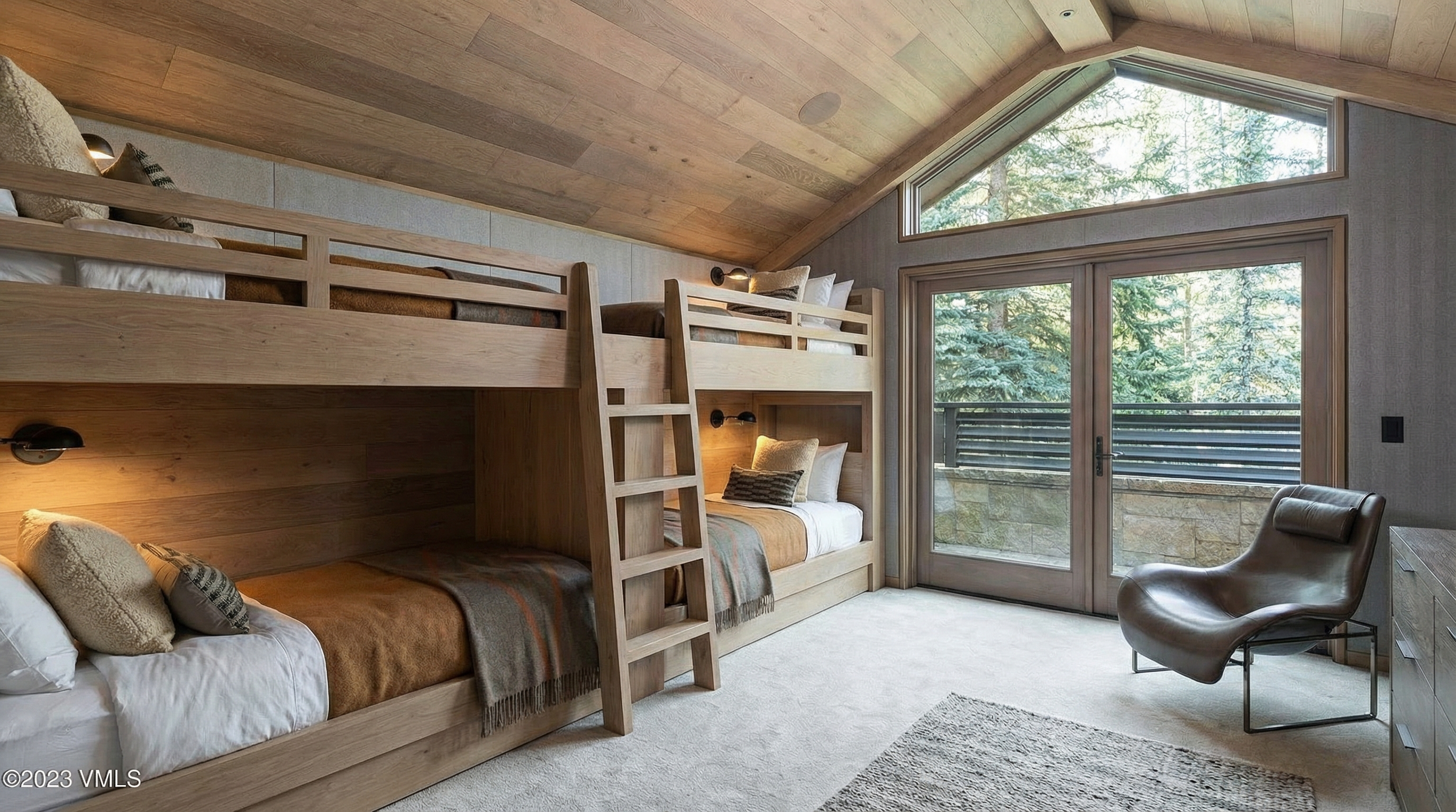 This is a bedroom featuring built-in bunk beds. The room has a warm, rustic aesthetic with wood paneling on the walls and ceiling. Large windows provide ample natural light and views of the outdoors.