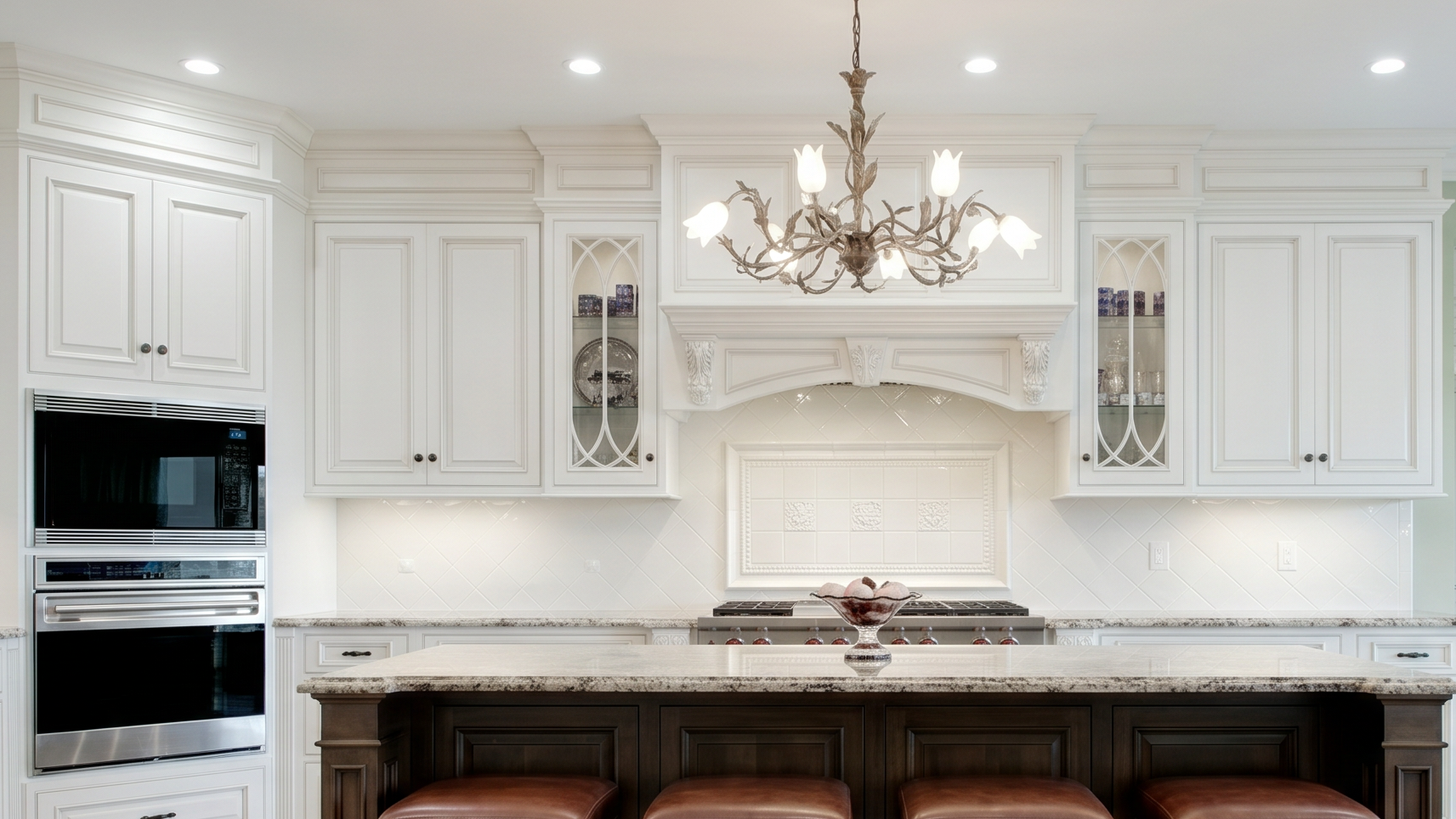 This elegant and spacious kitchen features high-end white cabinetry, professional-grade stainless steel appliances, and a prominent range hood area with detailed tile work. A large dark-toned kitchen island with leather stools serves as a central focal point, while a distinctive chandelier adds a touch of classic sophistication. The overall design is refined and luxurious, combining traditional architectural elements with modern functionality.