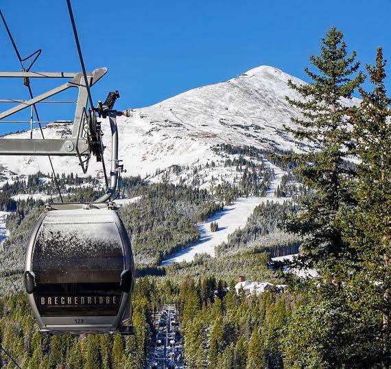 This image features a Breckenridge gondola car suspended in the air, offering a clear view of the surrounding snow-capped mountains and evergreen forest. The scene captures the picturesque outdoor recreation and scenic beauty that defines the Breckenridge area. It serves as an excellent amenity highlight for a property listing located in or near this popular mountain resort destination.