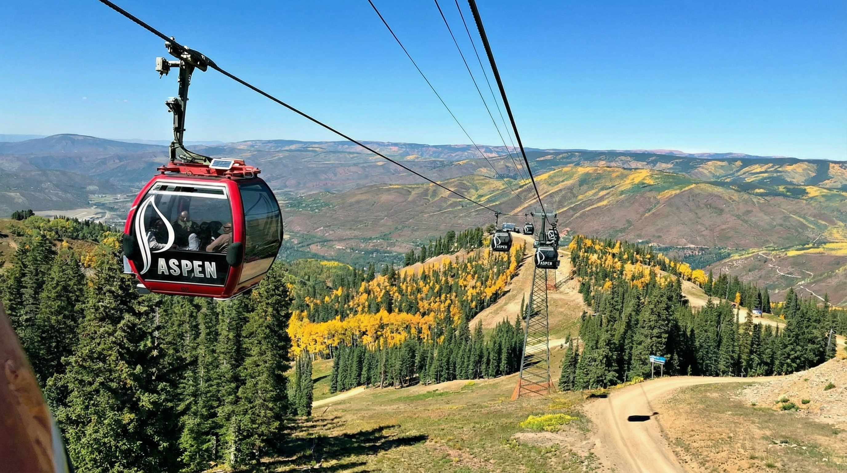 This stunning aerial view showcases the Aspen ski resort with its gondola lift system soaring over a landscape of lush trees and mountainous terrain. The clear blue sky and vibrant autumn colors create a picturesque scene. This image emphasizes the property's location within a popular recreation destination highlighting its proximity to outdoor activities.
