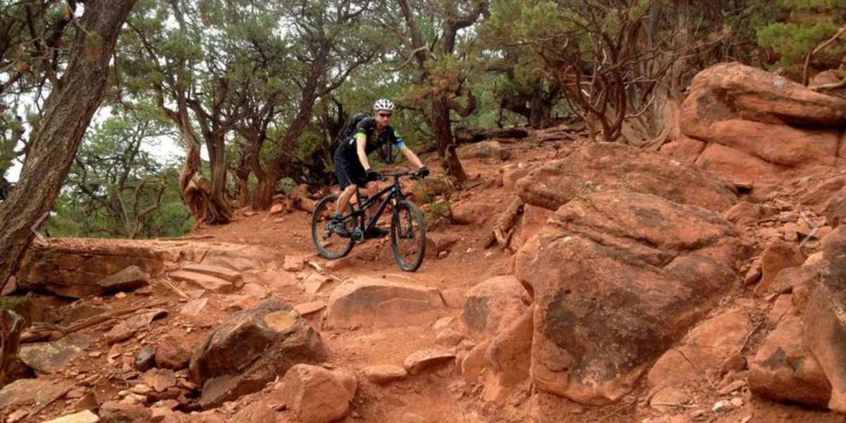 This image highlights a rugged, natural mountain biking trail set within a scenic, rocky woodland environment. The landscape features deep red soil and geological formations characteristic of desert or canyon regions, suggesting outdoor recreational access near a property. It showcases the area's natural beauty and potential for active outdoor lifestyles.