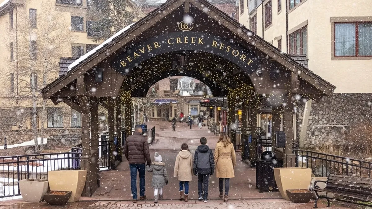 This image features the Beaver Creek Resort entrance, showcasing a covered walkway with the resort's name prominently displayed. The area is welcoming and well-maintained, suggesting a desirable and upscale community amenity. Festive lights and a family walking toward the entrance enhance the appealing atmosphere, making it ideal for attracting potential buyers interested in a resort lifestyle.