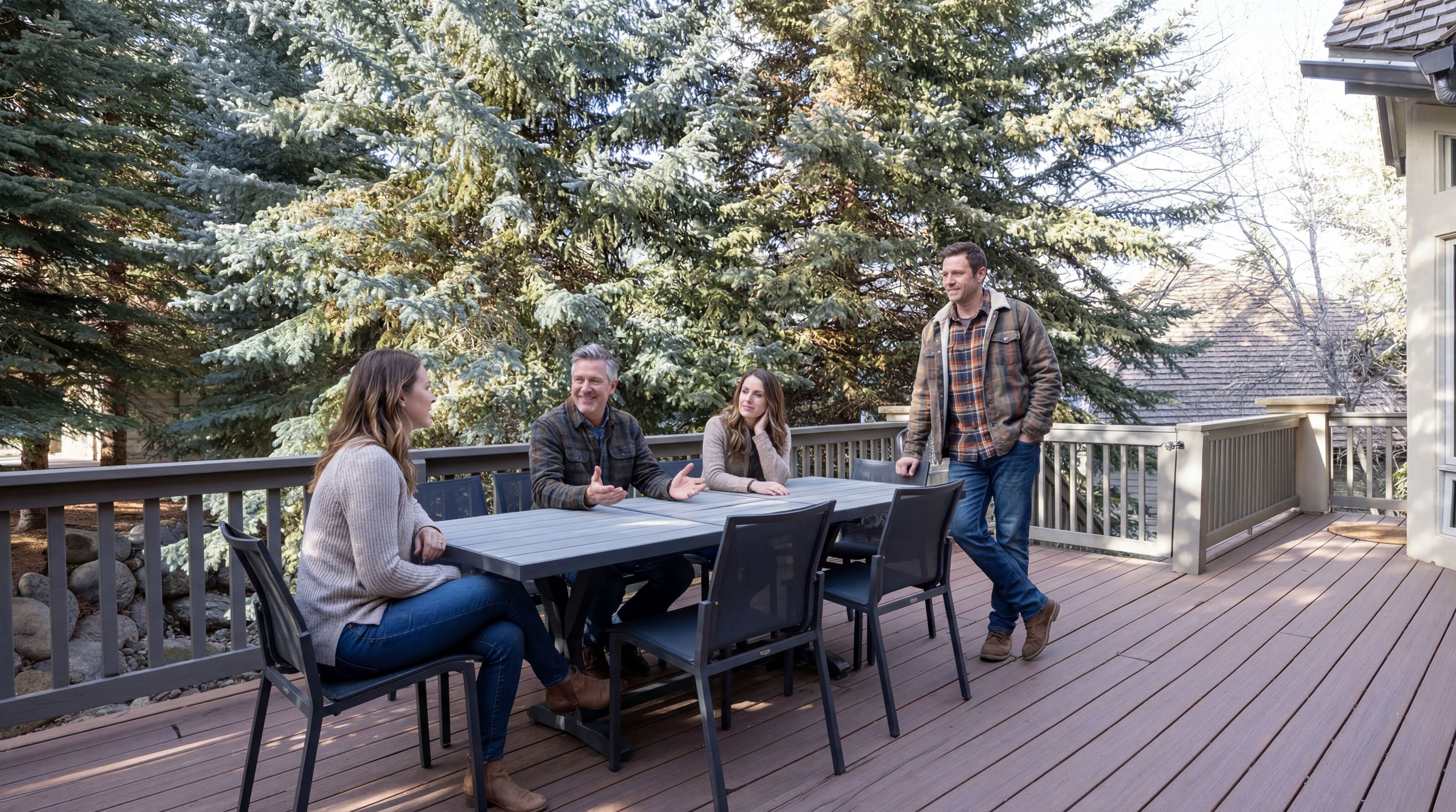 This outdoor deck offers a spacious, elevated area ideal for entertaining, featuring a large dining table and stylish mesh chairs. Surrounded by lush, mature pine trees, the space benefits from a natural and private atmosphere. The composite decking and quality railing ensure a low-maintenance, polished look perfect for relaxed outdoor living.