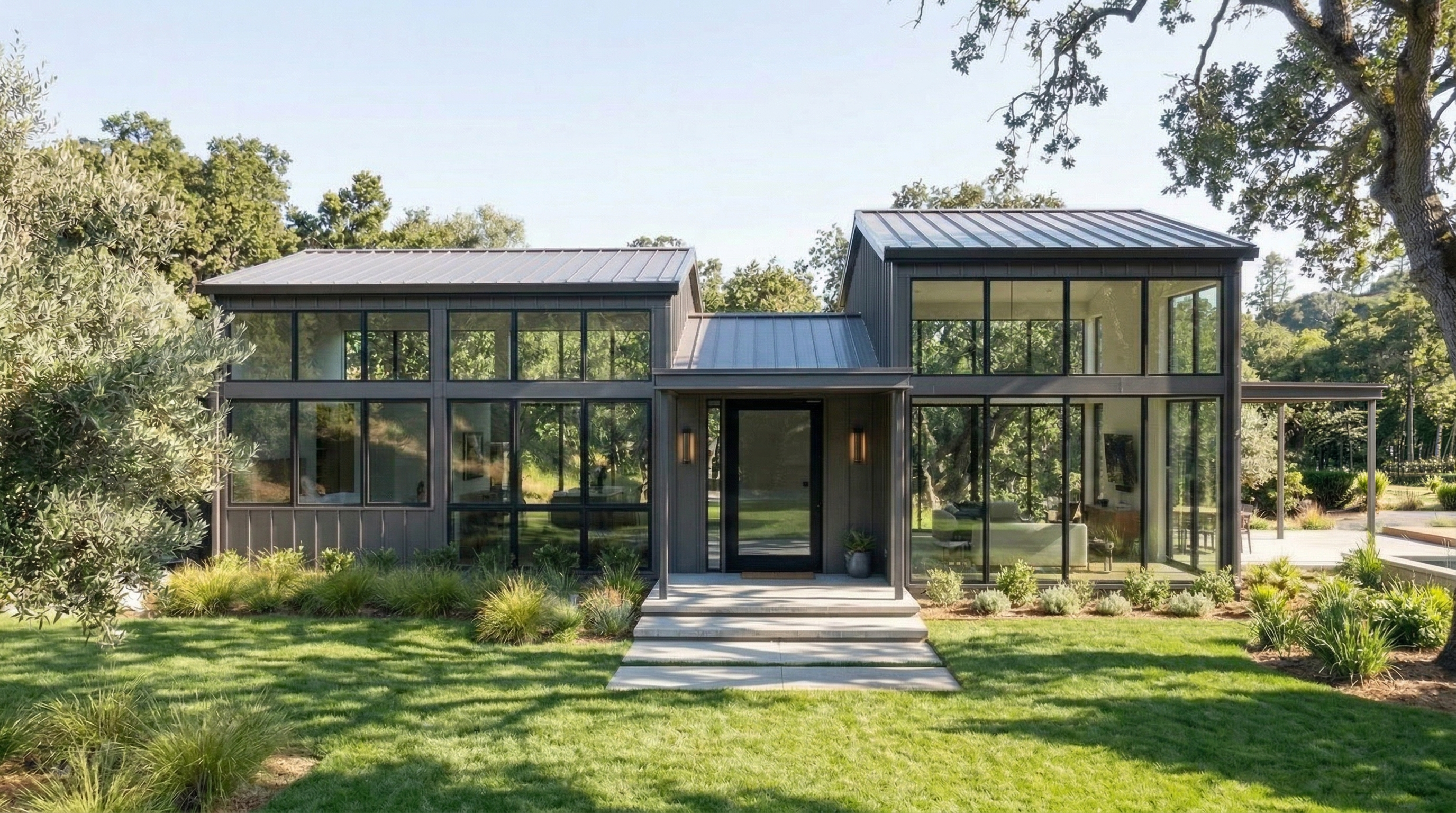 This modern, single-story architectural home features a striking combination of dark vertical paneling and expansive floor-to-ceiling windows that seamlessly blend indoor and outdoor living. The symmetrical design is centered by a sleek, covered entry with stone steps, set against a manicured lawn and lush, native-inspired landscaping. Its sophisticated, minimalist aesthetic offers excellent curb appeal with a contemporary, high-end feel.