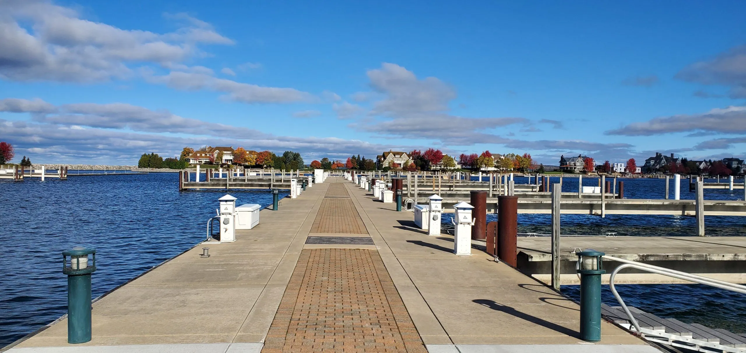 This image showcases a well-maintained marina dock extending out into a tranquil body of water, offering residents convenient access to boating activities. The dock features paved walkways with integrated lighting and clear paths, framed by attractive homes and vibrant autumn foliage in the background. It provides a peaceful and picturesque outdoor amenity that enhances the lifestyle appeal of the waterfront community.