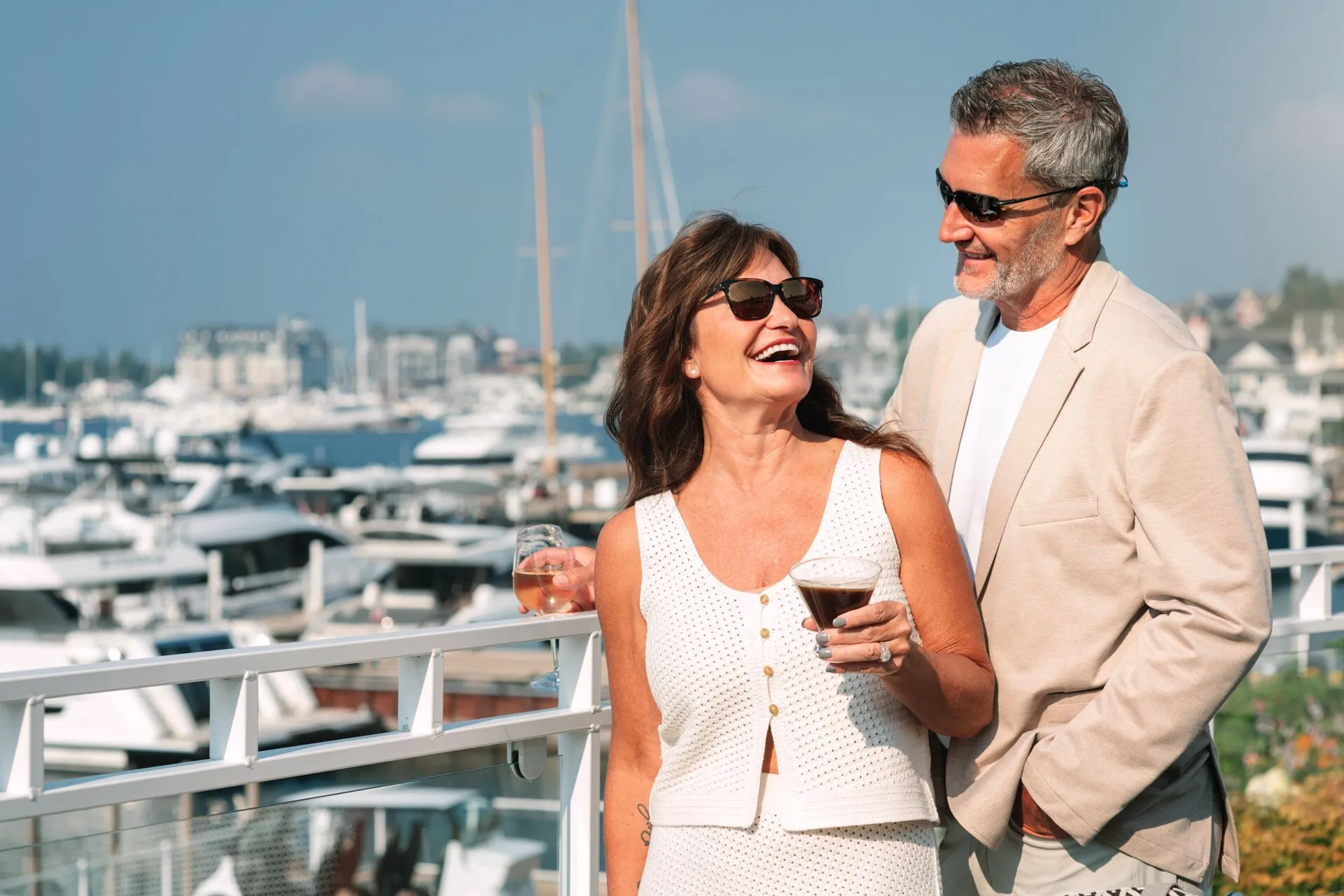 This image features a couple enjoying a scenic balcony overlooking a marina filled with yachts and boats. The balcony is equipped with a white railing and offers a clear, elevated view of the waterfront, suggesting a luxury lifestyle or high-end residential amenity. The setting conveys an inviting, relaxing atmosphere perfect for leisure and socialization.
