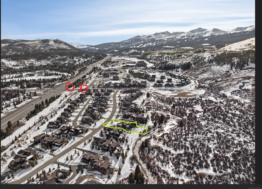 This aerial shot presents a residential community nestled in a snowy, mountainous landscape. The houses are clustered together, suggesting a cohesive neighborhood. There are some streets winding through community.