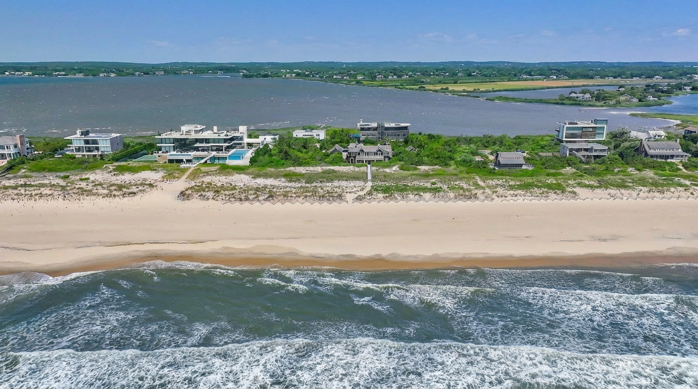 This aerial view showcases luxury beachfront properties with modern architecture and stunning ocean access. The properties feature well-manicured lawns, private access to the beach, and expansive water views. The scene evokes a sense of exclusivity and high-end living.
