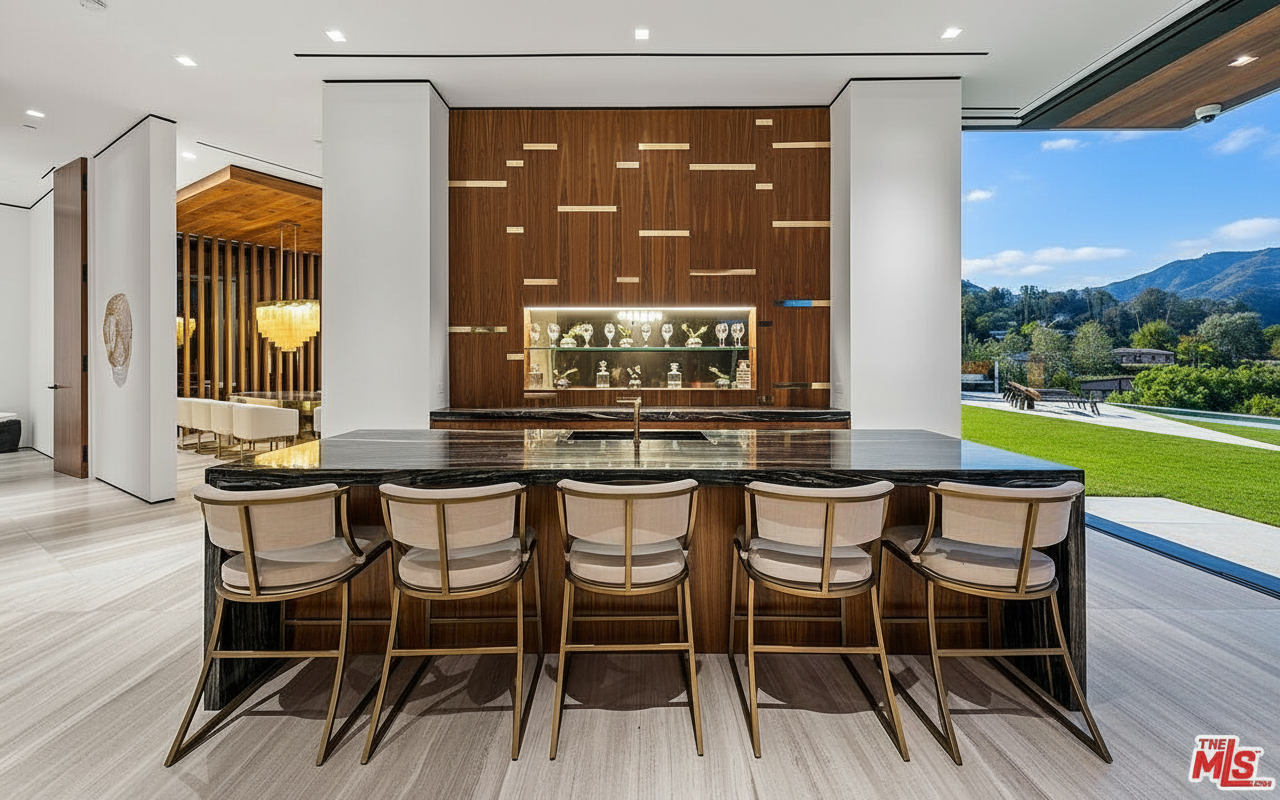This interior shot focuses on a stylish kitchen bar area with five stools, a marble countertop, and a wooden accent wall. The adjacent outdoor space and greenery are visible through a large window, adding to the bright and modern ambiance. The overall impression is luxurious and well-designed, suggesting a high-end property.