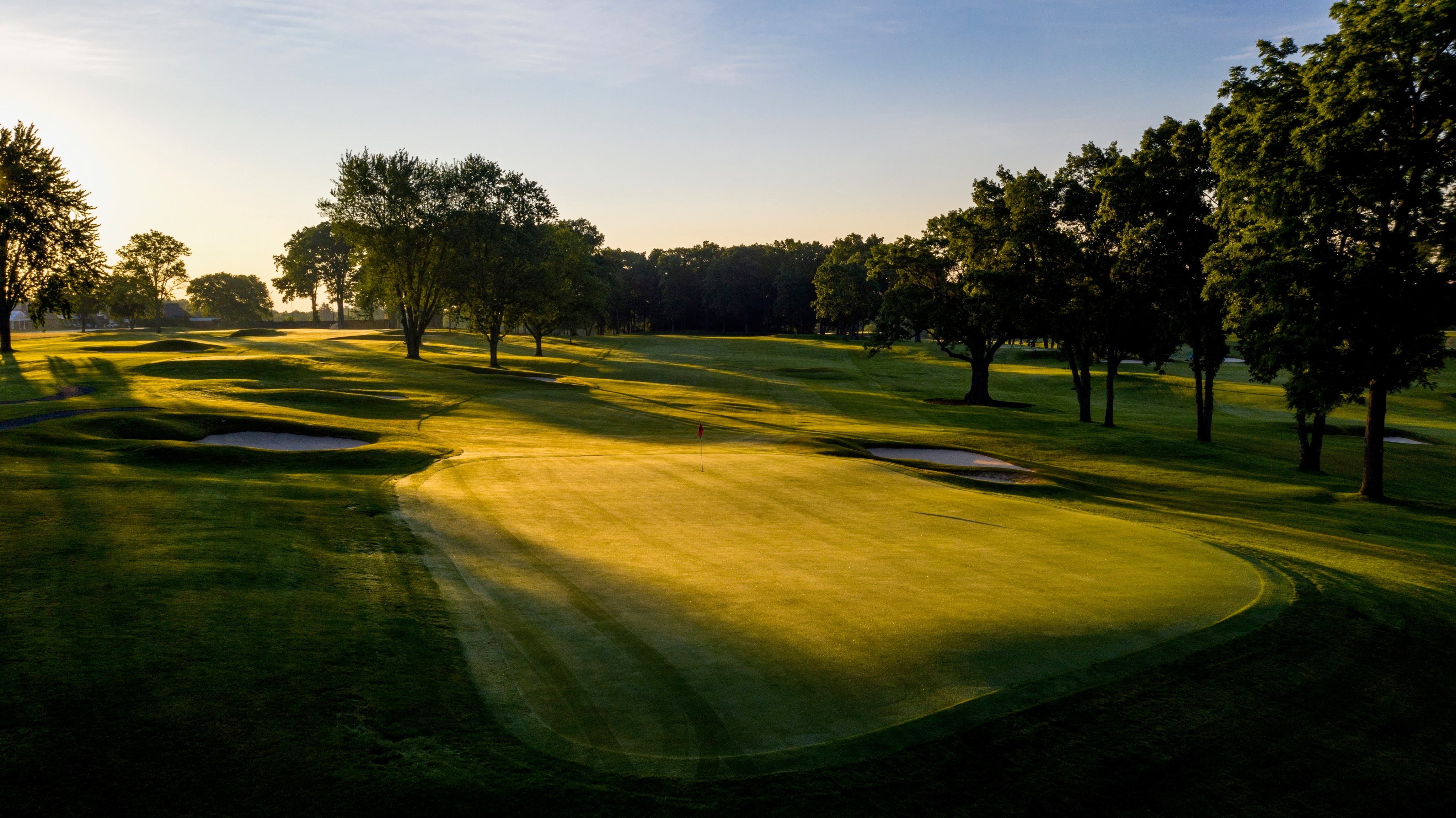 This aerial view showcases a meticulously maintained golf course with lush green fairways and greens. Mature trees line the course, and sand bunkers add to the challenge and aesthetic appeal. The scene evokes a sense of luxury and tranquility, highlighting the property's recreational potential and desirable location.