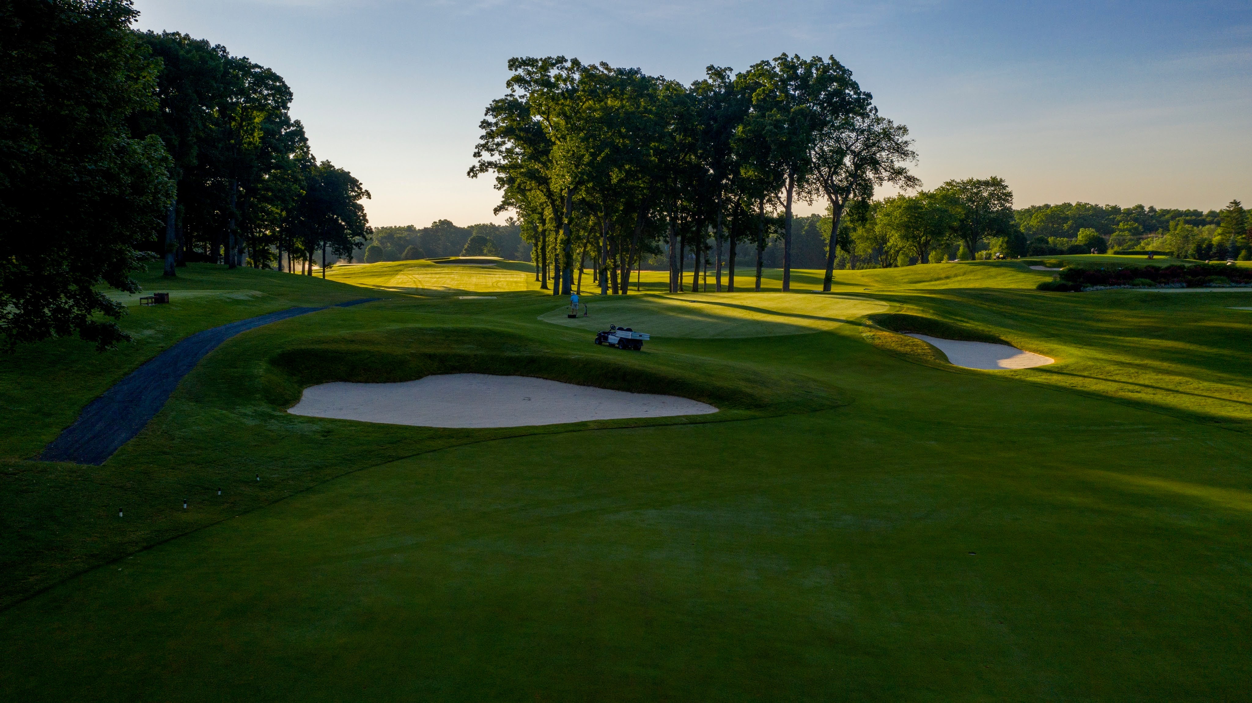 This image showcases a beautifully maintained golf course, highlighting its use as an expansive yard/garden space. The manicured green is complemented by sand traps, trees, and a winding path, creating an appealing outdoor environment. The photo suggests a tranquil and luxurious lifestyle, ideal as an amenity for a high-end property.
