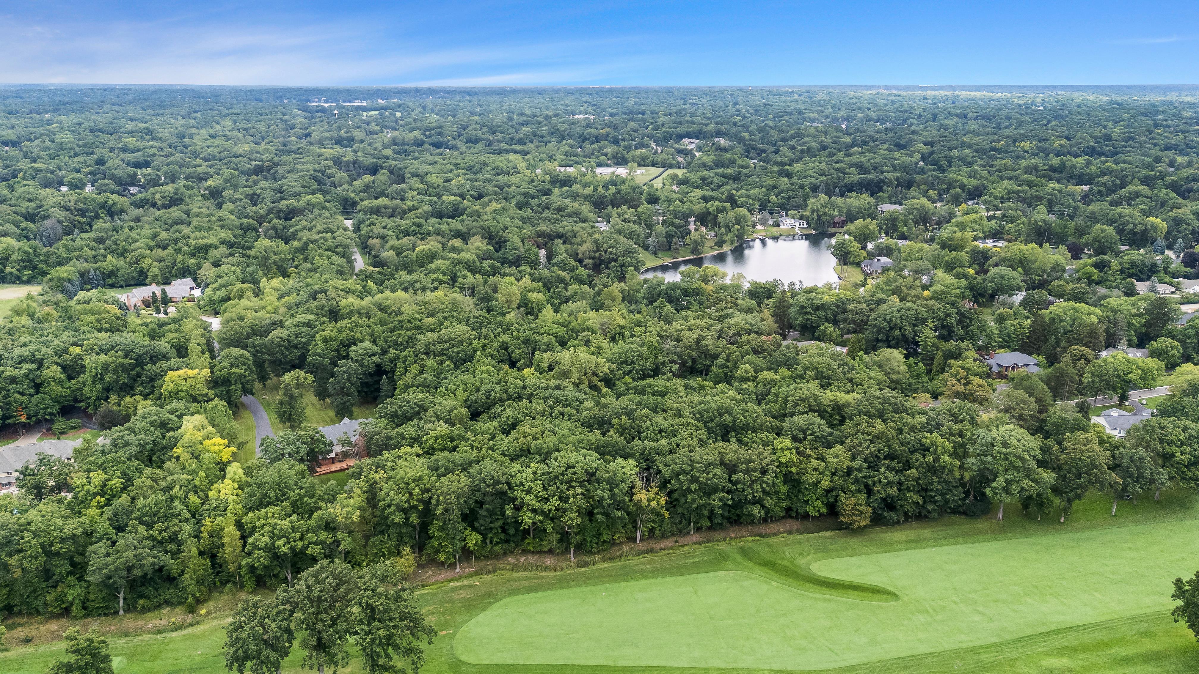 This aerial view showcases a luxurious residential landscape. A well-maintained golf course feature is visible, surrounded by lush, mature trees. In the distance lies a serene lake, enhancing the property's appeal and suggesting privacy and exclusivity.