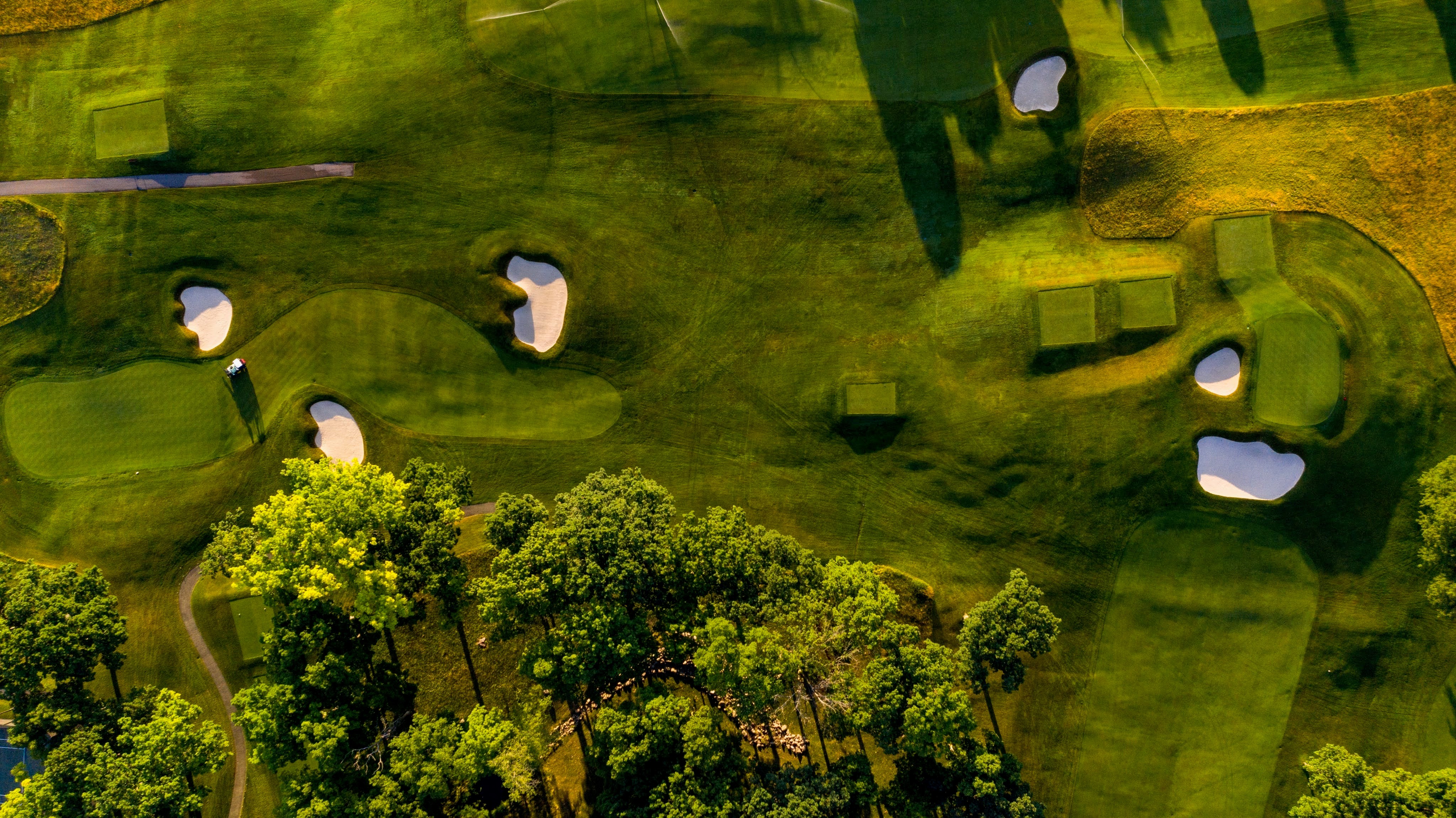 An aerial view showcases a meticulously maintained golf course, featuring lush green fairways, strategically placed sand traps, and mature trees. The image highlights the expansive and manicured landscape, representing an attractive amenity for a luxury property or community. The scene is bathed in warm sunlight, emphasizing the beauty and tranquility of the setting.