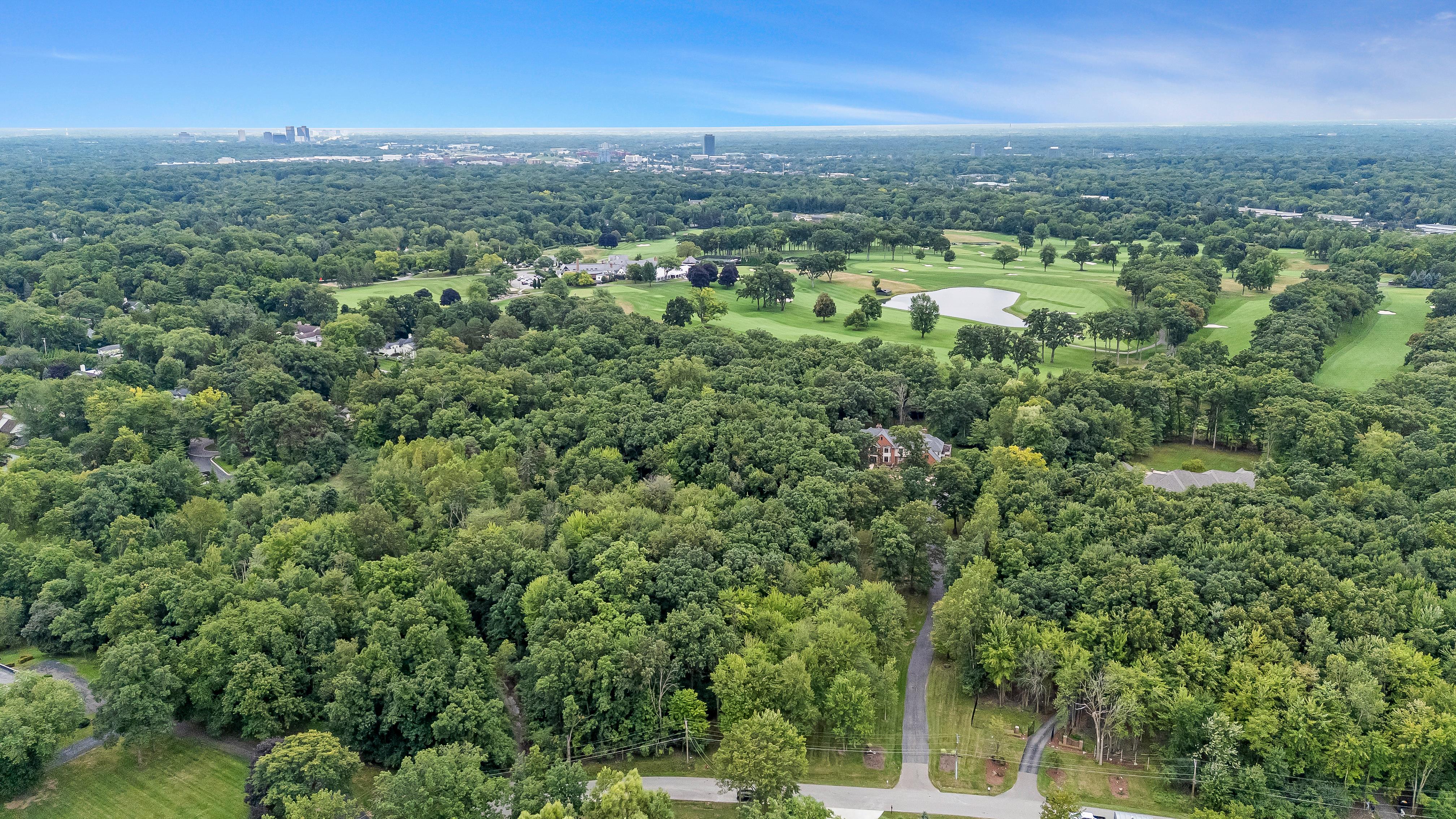 This aerial view showcases a sprawling residential area interspersed with lush greenery and a well-manicured golf course. The image provides a sense of the property's expansive surroundings and proximity to recreational amenities. In the distance, a cityscape adds an element of urban accessibility.