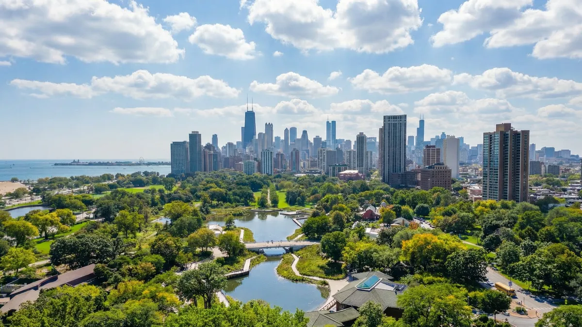This aerial view showcases a vibrant cityscape with numerous high-rise buildings, presumably residential and commercial. Lush greenery and a scenic park with a winding lake and walking bridge are prominent in the foreground, creating a balanced and aesthetically pleasing composition. The image emphasizes the proximity of nature to urban living, making it attractive to potential buyers seeking both city life and access to outdoor recreation.