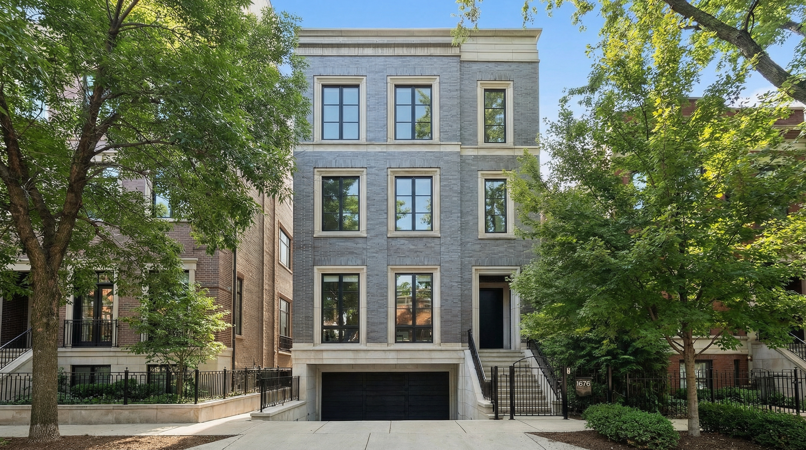 This image showcases the front facade of a modern-style three-story townhouse. It has a gray brick exterior with black-framed windows and a black garage door. The property features a symmetrical design with a well-maintained front yard and landscaping, enhancing its curb appeal.