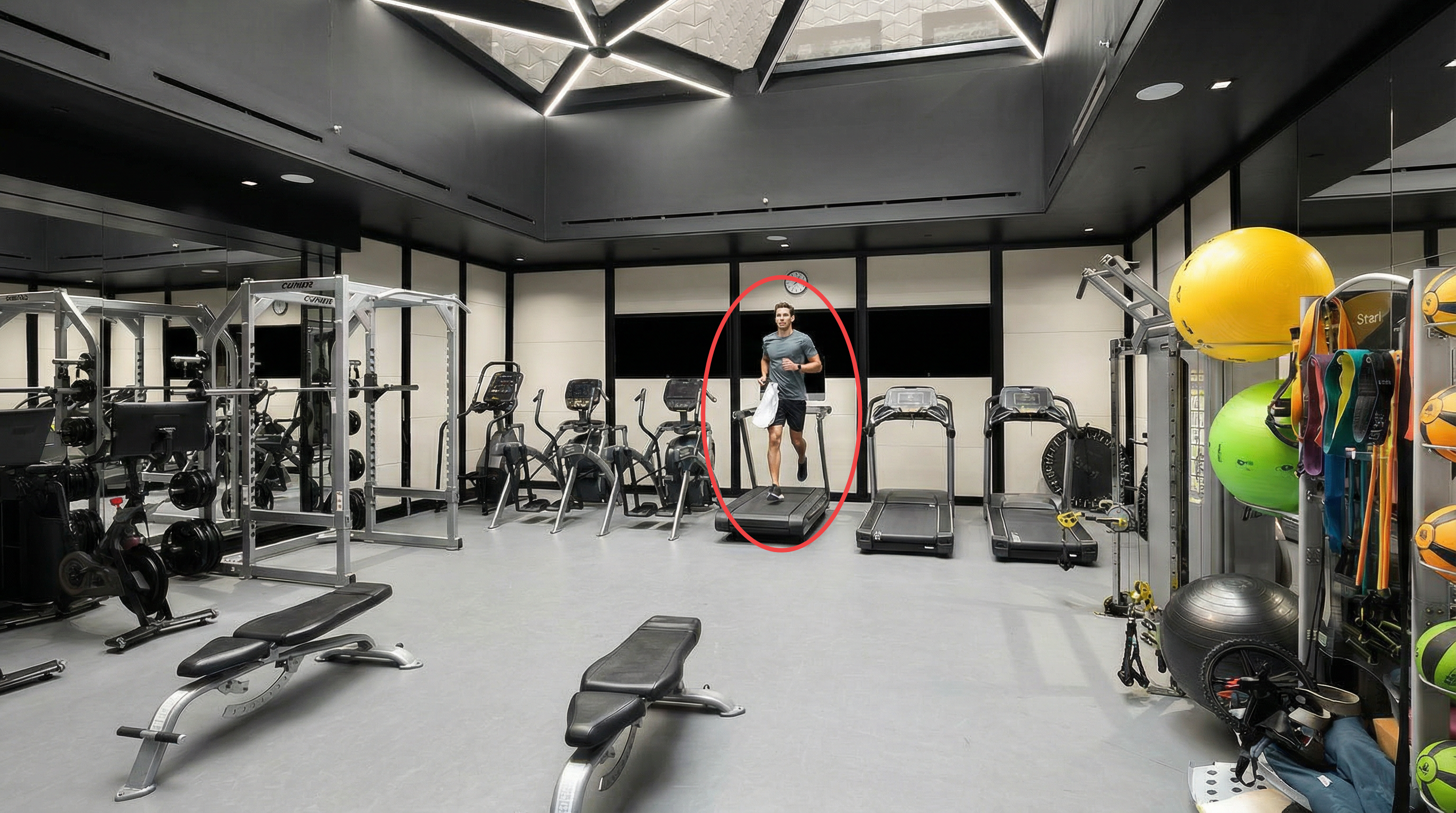 This modern, well-equipped personal home gym features a sleek fitness area with multiple treadmills, ellipticals, and strength-training equipment. The space is illuminated by a unique, geometric skylight, creating a bright and professional atmosphere that suggests a high-end luxury residential facility.
