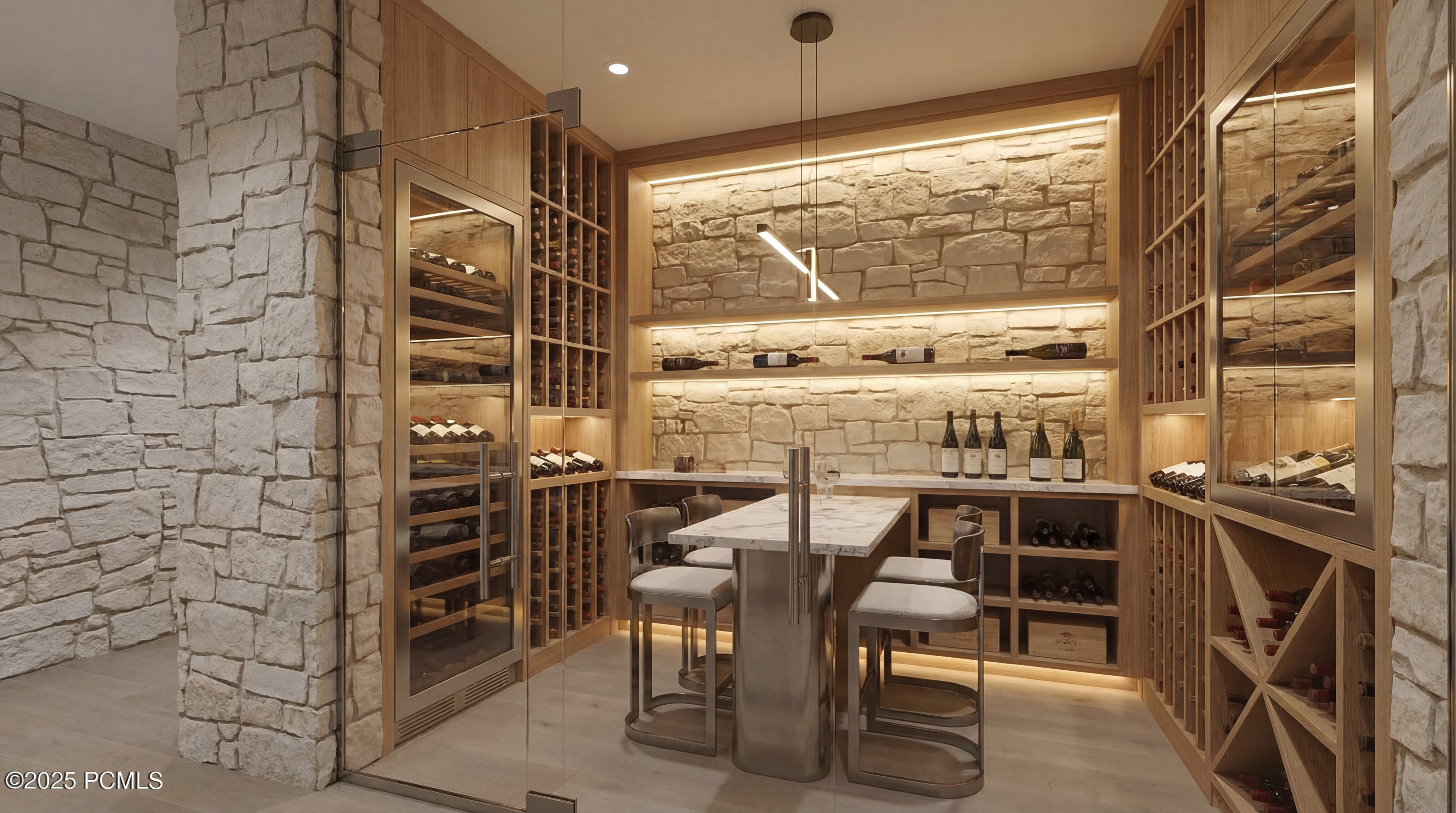 This is an interior shot of a well-appointed wine cellar. The space features stone accent walls, wooden wine racking systems, a glass-enclosed wine refrigerator, and a small table with chairs for tasting. The lighting is warm and highlights the textures of the materials used, creating an inviting ambiance.