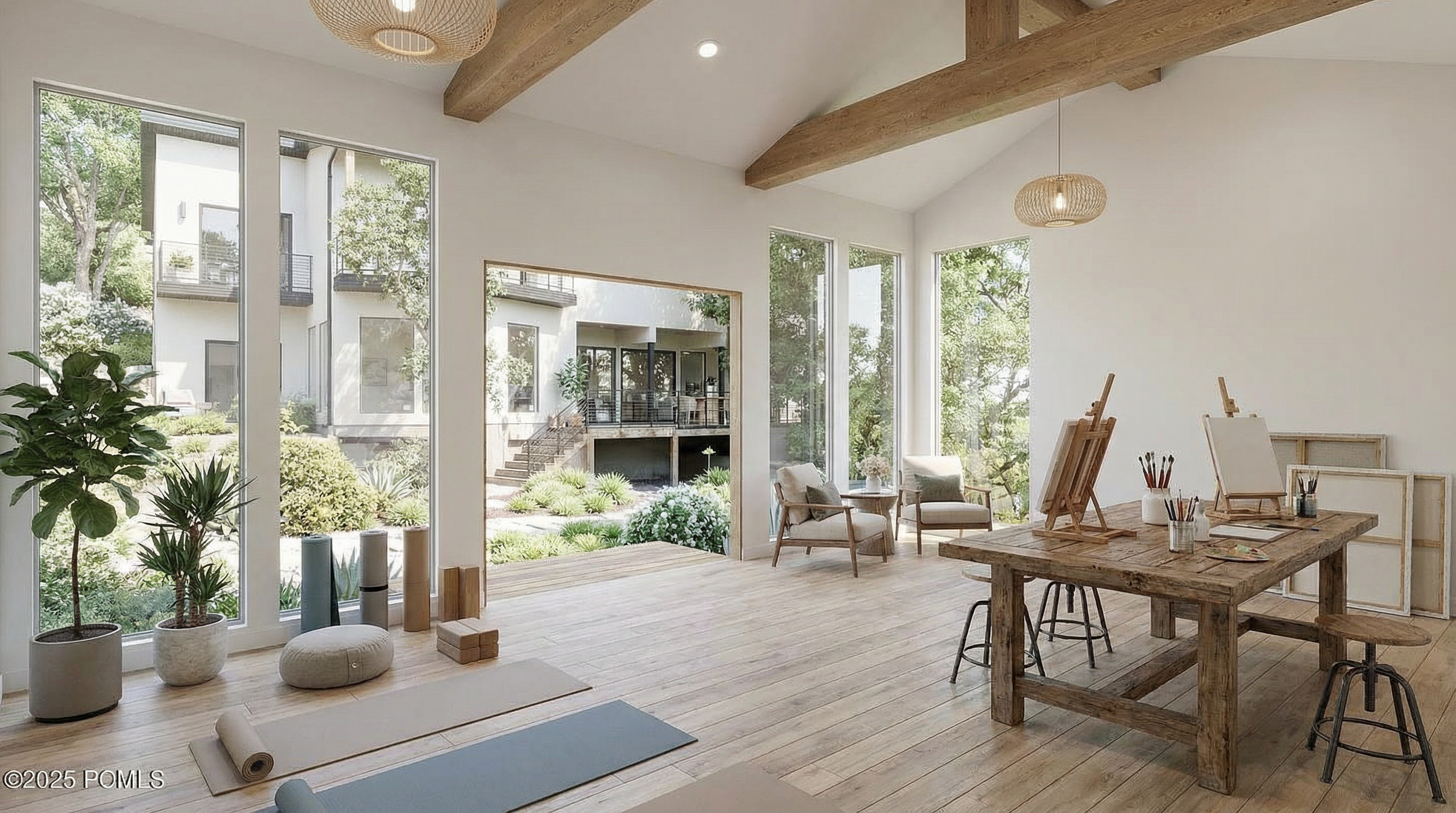 This inviting space is designed as a home gym and/or art studio with hardwood floors, exposed beams, and natural light pouring in through large windows overlooking the landscape. Yoga mats, stools, tables, paint brushes, and easels suggest a versatile area for both physical and creative activities. The peaceful setting contributes to a relaxing atmosphere suitable for exercise and artistic pursuits.