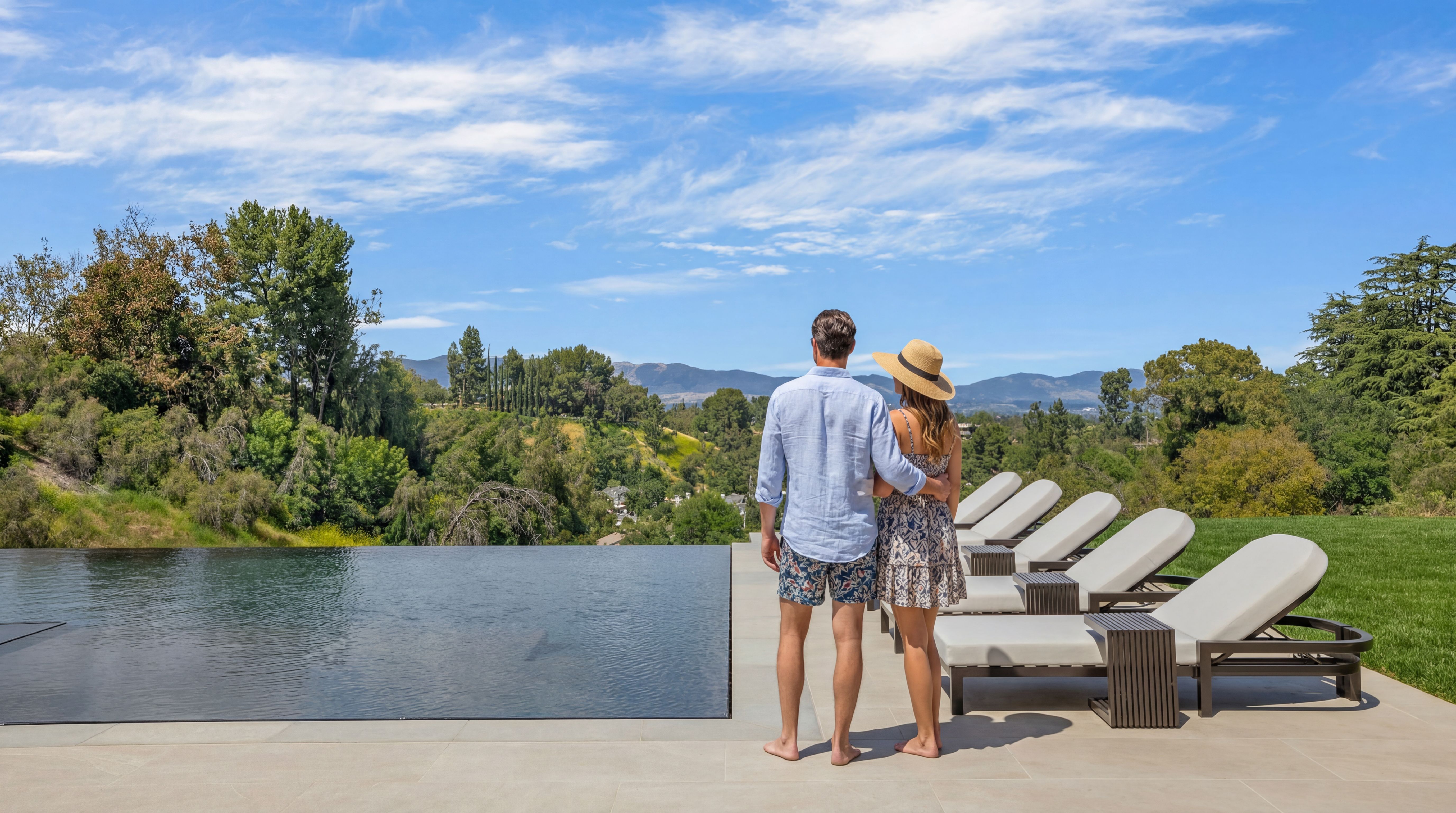 This stunning outdoor space features an elegant infinity-edge swimming pool overlooking a lush, rolling hillside and mountain landscape. The expansive stone patio is furnished with multiple modern lounge chairs, creating a serene and luxurious atmosphere for relaxation and breathtaking views. The scene perfectly highlights the high-end residential appeal of this private, resort-like terrace.