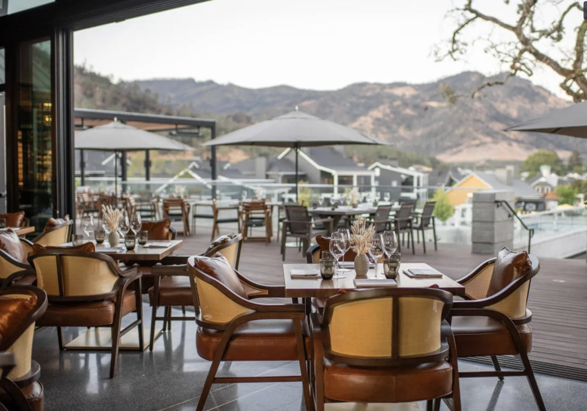 This spacious, open-air terrace offers a sophisticated outdoor dining experience with upscale bistro-style seating and tables. The area features sweeping views of the surrounding mountains and nearby buildings, creating a high-end, resort-like atmosphere ideal for entertaining. The seamless transition between the indoor and outdoor environments highlights the property's refined architectural design and excellent functional flow.