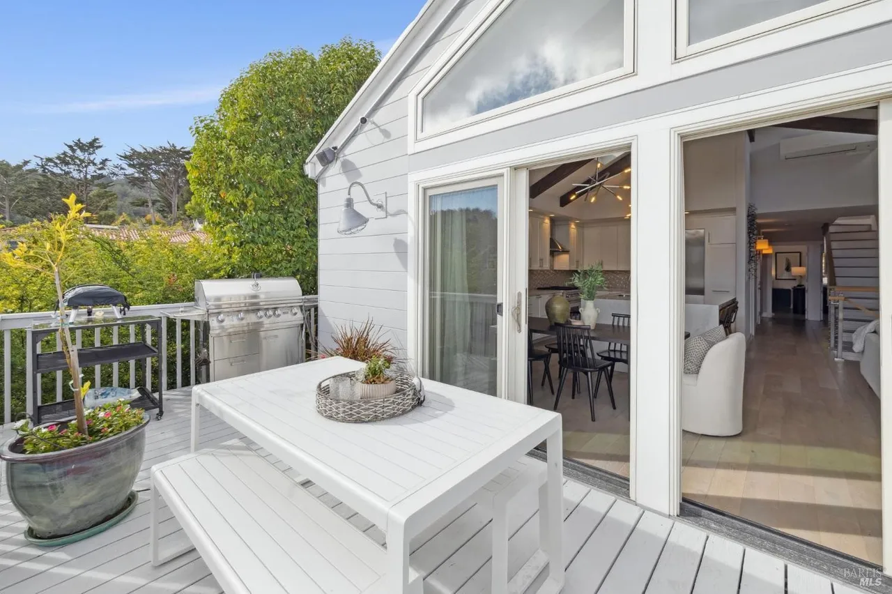 This image showcases a charming outdoor deck area, perfect for entertaining or relaxing. The deck features a white dining set, including a table and bench, along with a grill, suggesting a space designed for outdoor dining. Sliding glass doors provide seamless access to the home's interior, creating an inviting indoor-outdoor flow.