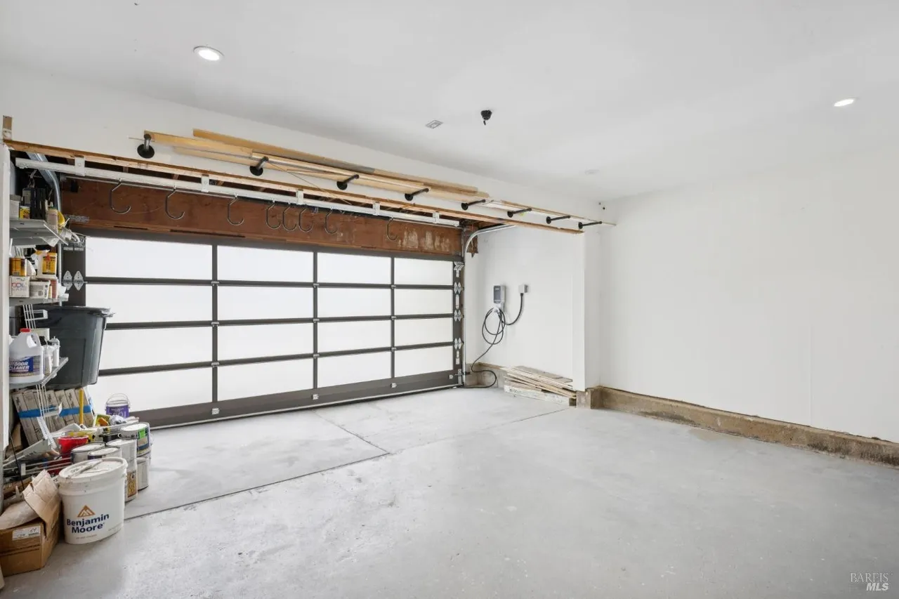 The image showcases a spacious garage interior with a modern, partially open garage door featuring horizontal panels. The concrete floor is clean and well-maintained, and the walls are painted in a neutral tone. Shelving and storage solutions are visible on the left, suggesting functionality and organization.