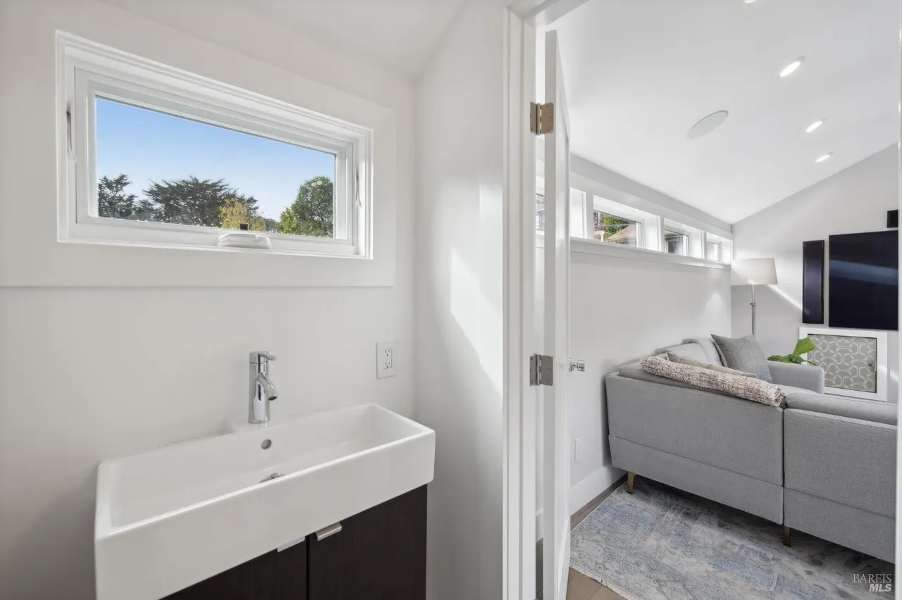 This image showcases a modern guest bathroom with a sleek, wall-mounted sink and dark cabinetry. A window provides natural light and a view of the outdoors. The bathroom opens into a living area, creating a sense of spaciousness and contemporary design.