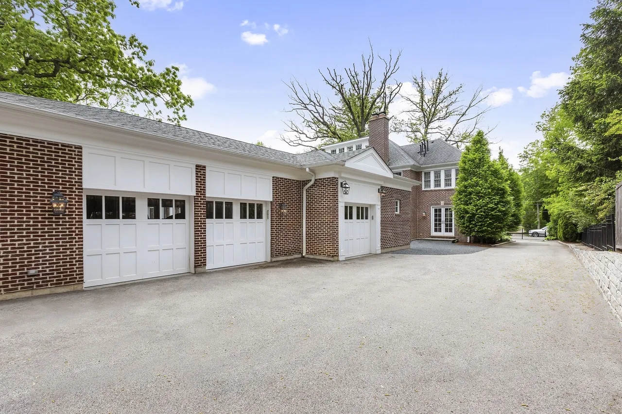 This image showcases a well-maintained brick garage with multiple white doors, suggesting ample parking and storage space. The driveway is spacious and leads to the main house, which is partially visible in the background. The overall impression is one of a functional and aesthetically pleasing exterior feature, enhancing the property's value.