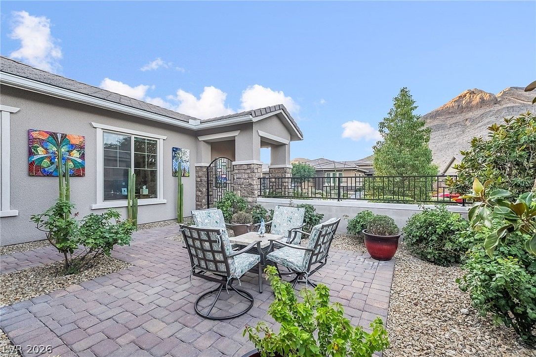 This outdoor living space features a paver patio furnished with a small fire pit and four metal-framed swivel chairs, perfect for enjoying the views. The area is surrounded by desert landscaping, including cacti and shrubs, and is enclosed by a decorative iron fence with a mountain backdrop. The space feels private, well-maintained, and ideal for relaxing or entertaining in a scenic, desert-inspired setting.