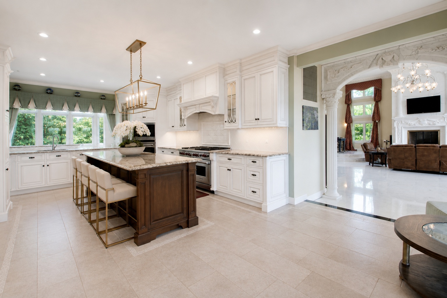 This elegant, high-end kitchen features white custom cabinetry paired with a rich, dark-stained wood island that includes integrated bar seating. Notable design elements include professional-grade stainless steel appliances, premium granite countertops, and sophisticated pendant lighting. The space offers a seamless, open-concept flow into the adjacent living area, which is highlighted by a grand arched entryway and luxurious architectural detailing.