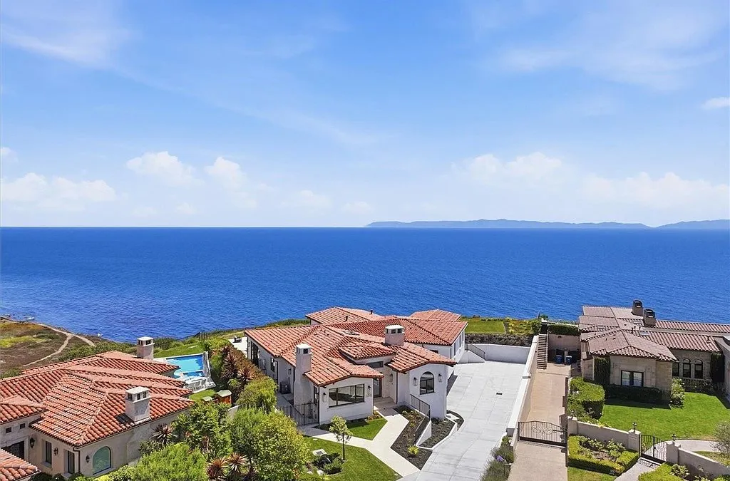 This stunning high-angle aerial view captures a premier coastal estate featuring multiple Spanish-style homes with red tile roofing. The property showcases expansive ocean views, a private swimming pool, and a meticulously landscaped layout. It is an impressive example of luxury waterfront living characterized by traditional Mediterranean architecture and panoramic scenery.