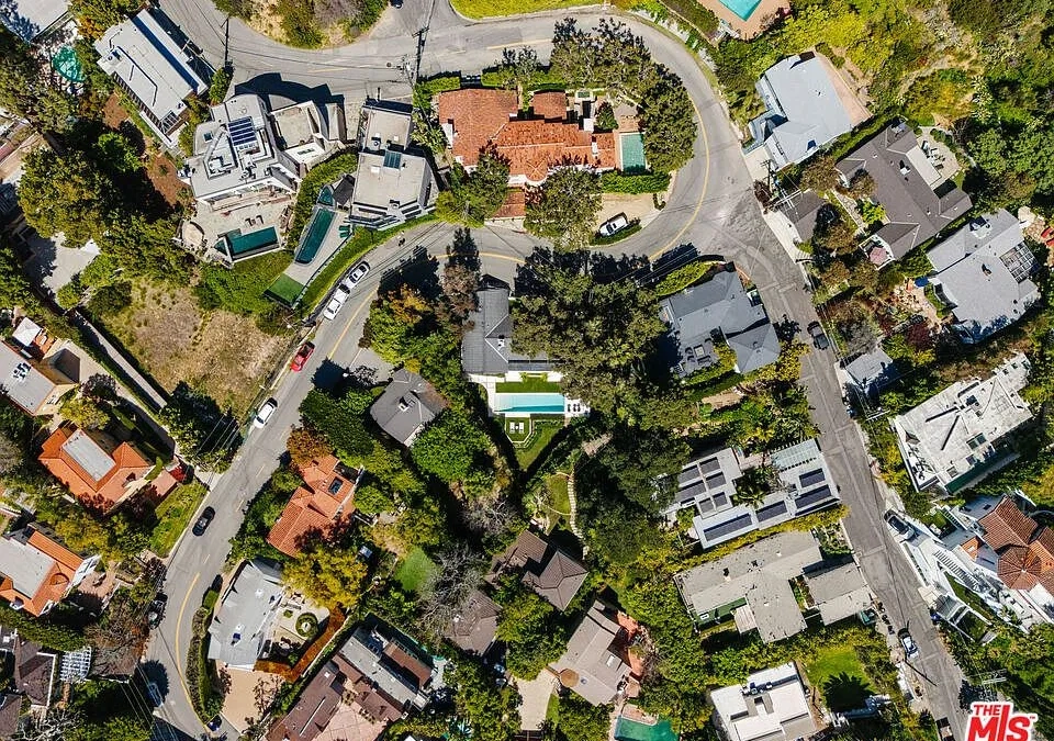 This aerial view showcases a collection of luxury homes in a lush neighborhood, highlighting the variety of architectural styles and landscaping. Several homes feature swimming pools, adding to the exclusive appeal. The image provides an overview of the area and its desirable residential setting.