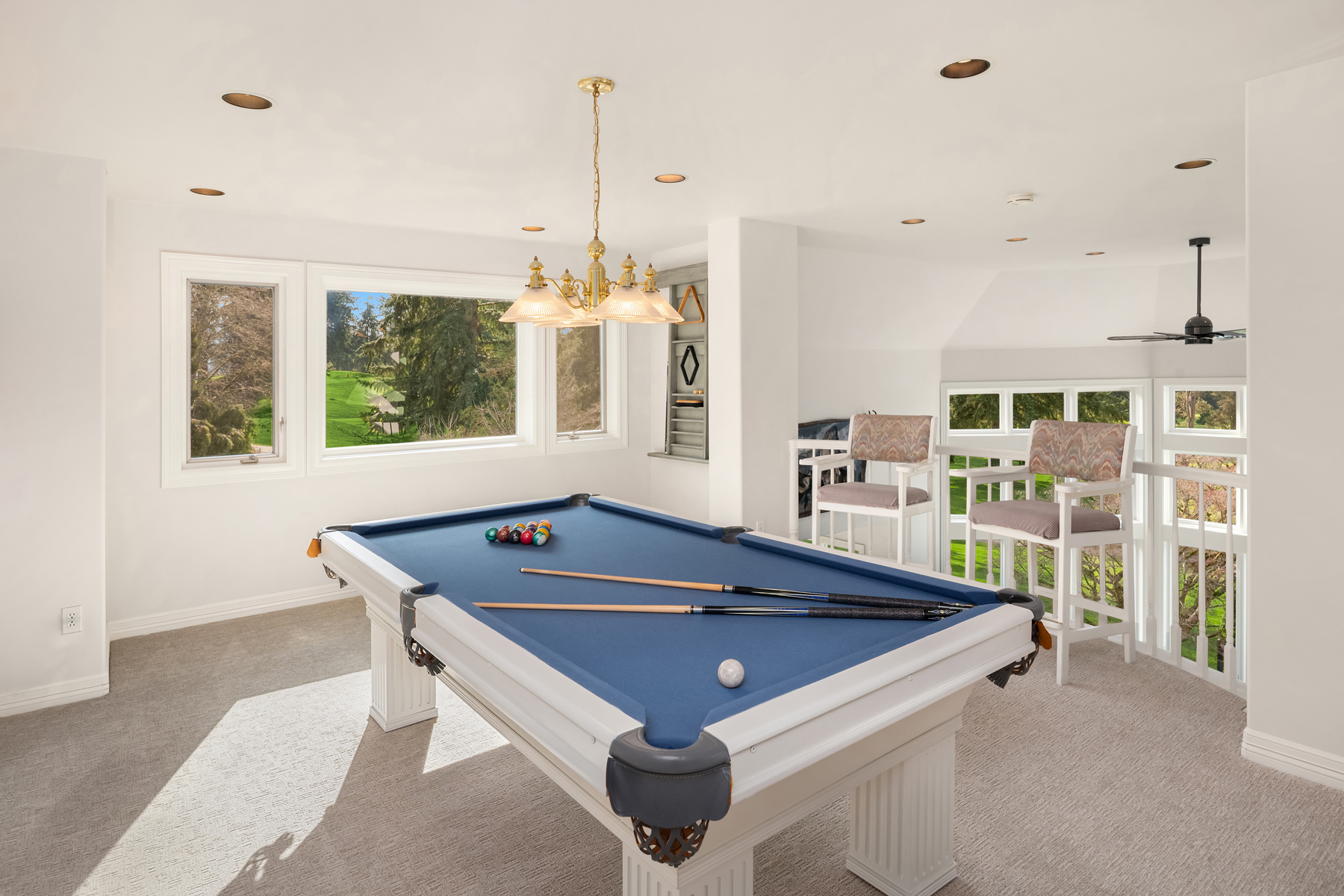 This interior shot showcases a well-lit living room featuring a pool table as a central element. The room is bright with natural light streaming through large windows, offering a view of the outdoors. The space is decorated in a neutral color palette, creating a clean and inviting atmosphere.